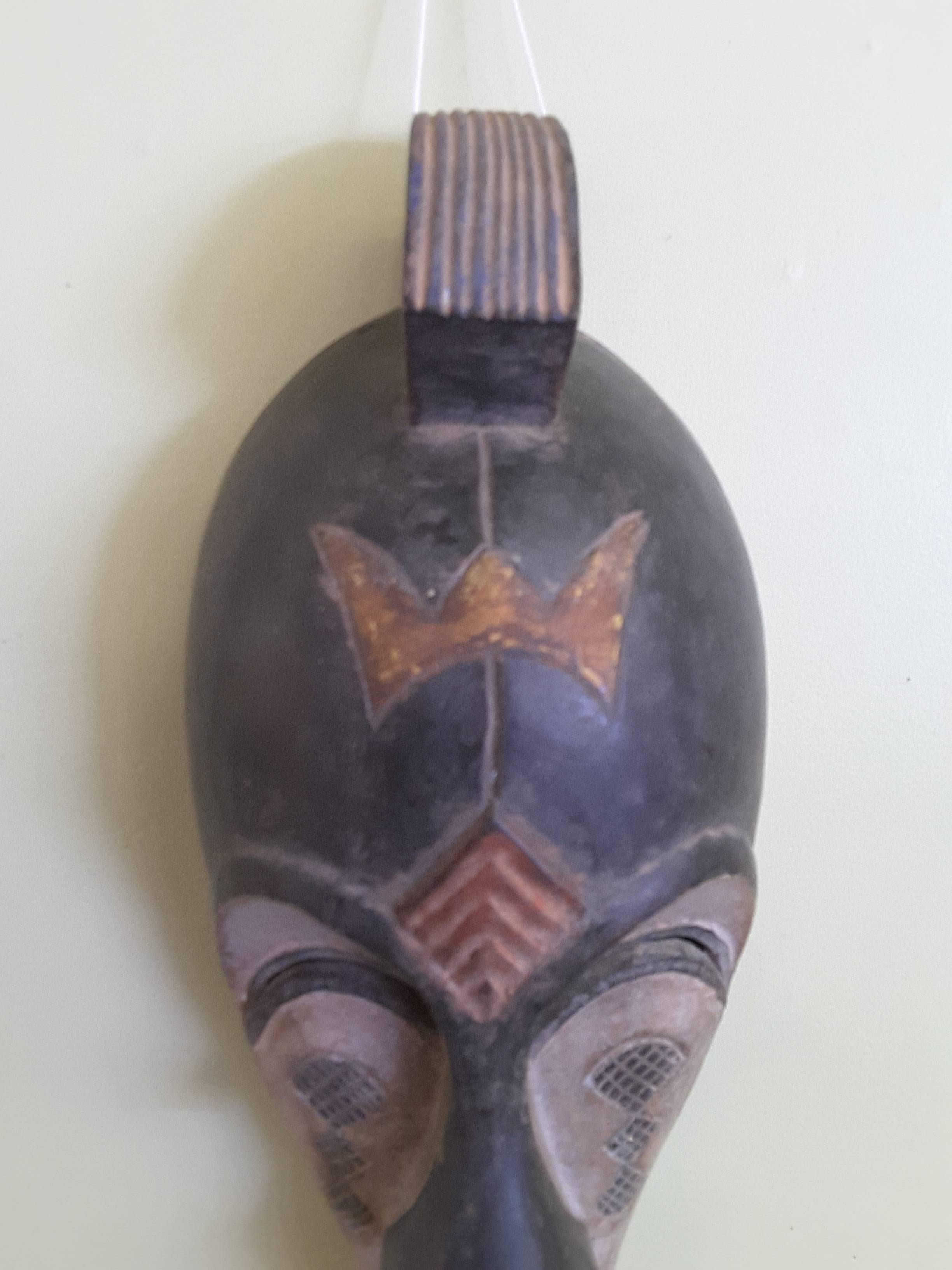 An African Gabon elongated tribal carved mask, paint decorated in black, off-white and rust brown. The top has center Horn type crown, the face is an exaggerated profile. The mask measures 19