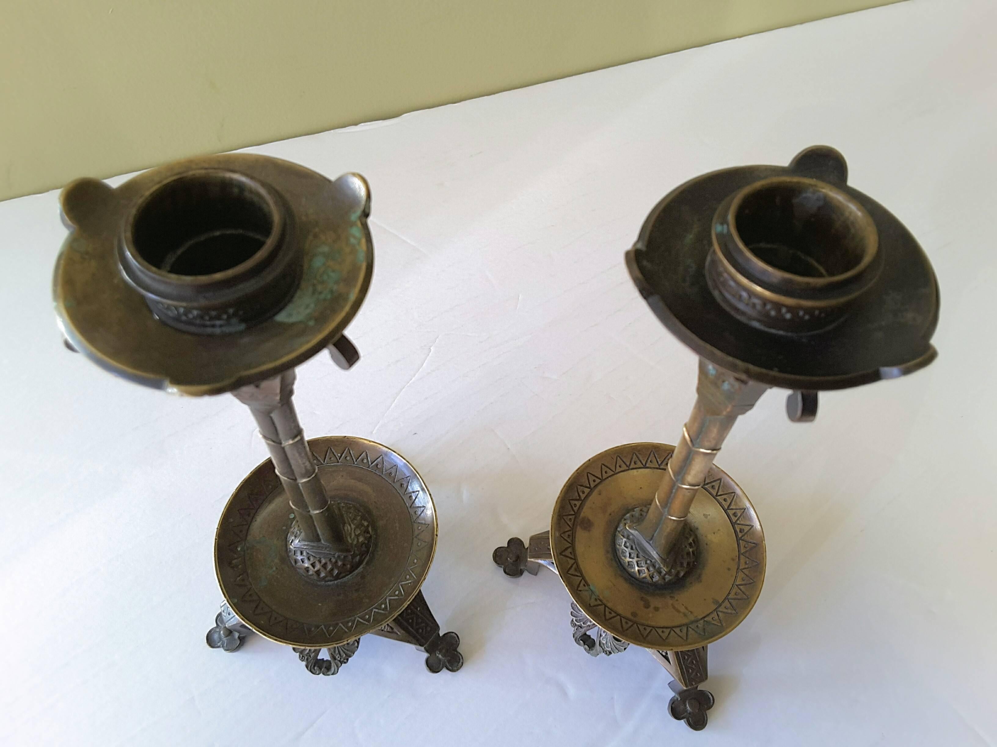 A pair of neo-gothic bronze candlesticks in the manner of Augustus Welby Northmore Pugin, finely cast in form of a gothic cluster column on a pierced tripod base. Aged patina with some verdigris. The candlesticks measure 8 1/4