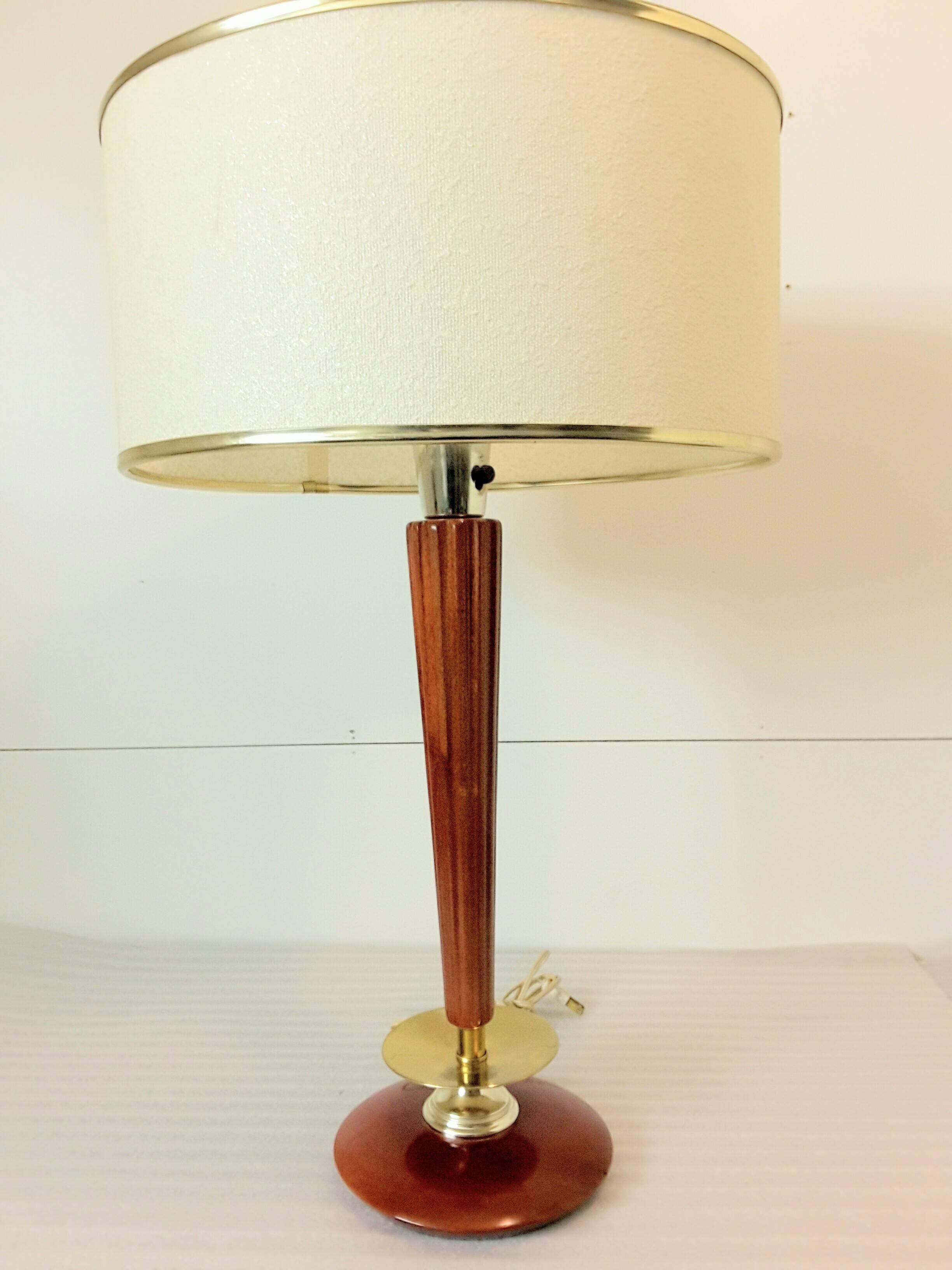 Mid-Century brass and mahogany Classic style table lamp, the lamp has a fluted tapered column to a raised brass disc above a mahogany base. Tri-light socket and a milk glass shade and comes with cloth shade which has accented brass colored edging.