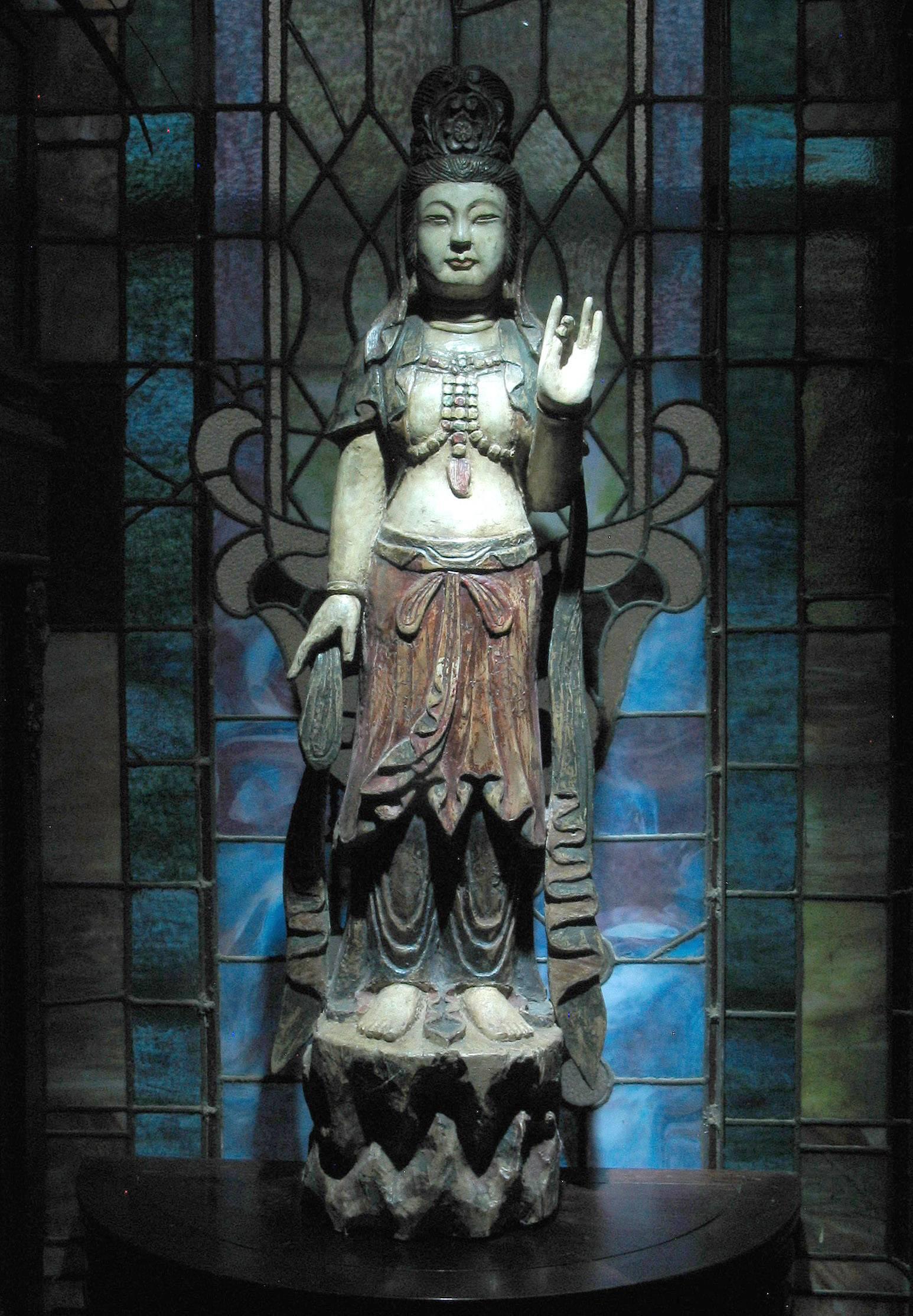A Chinese carved wood standing figure of Guanyin in the Ming dynasty style, with polychrome application, the hair tied back into an elaborate high chignon, with her left hand raised, holding a pearl and standing on a rock base.
Late Qing dynasty,