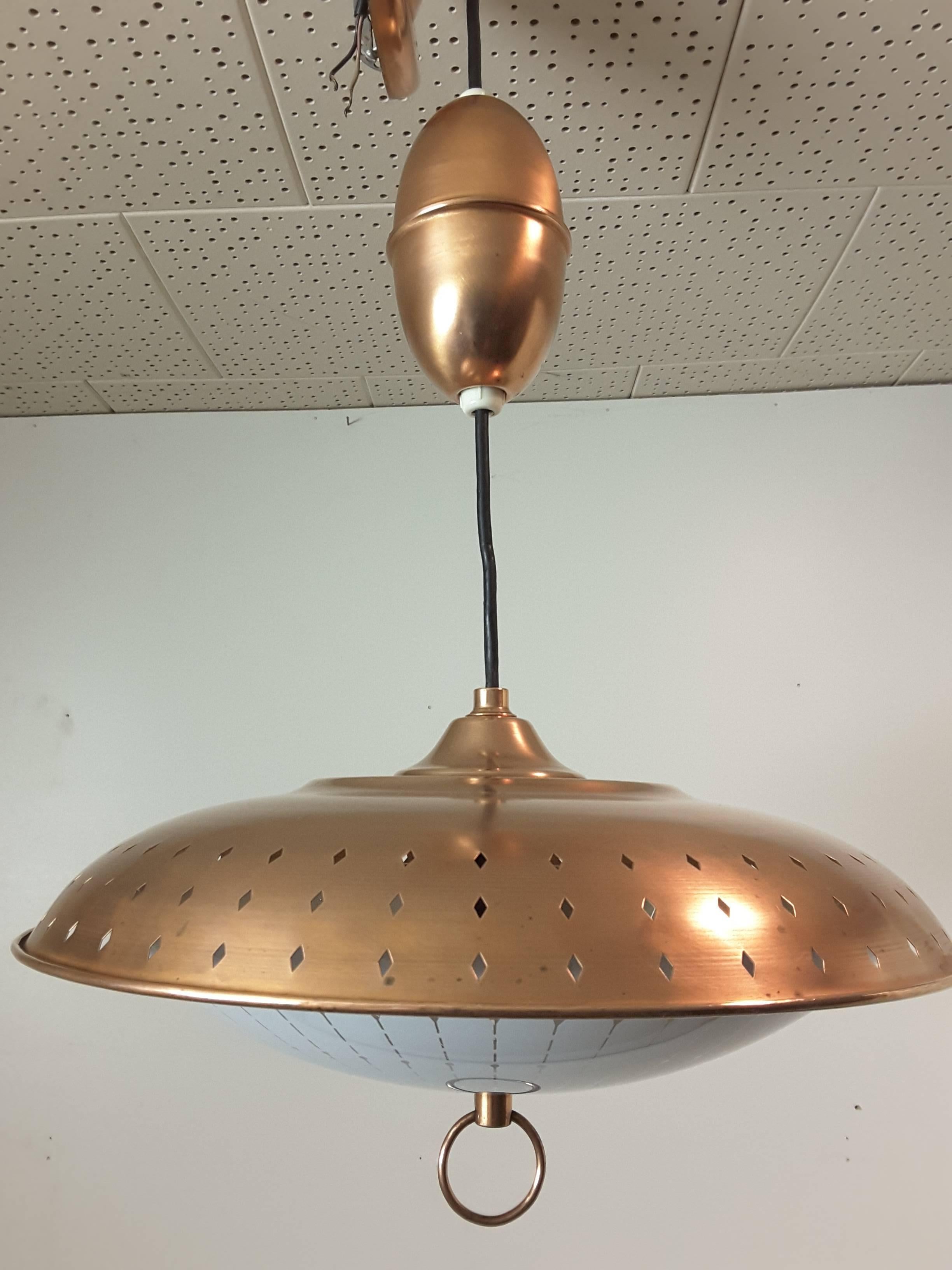 Mid-Century Gerald Thurston Solid Copper "Egg Pendant" retractable light fixture by Lightolier, circa 1950-1960's. The fixture is done in solid copper, with punched diamond shaped cut-outs for light on the top. The underside is a glass