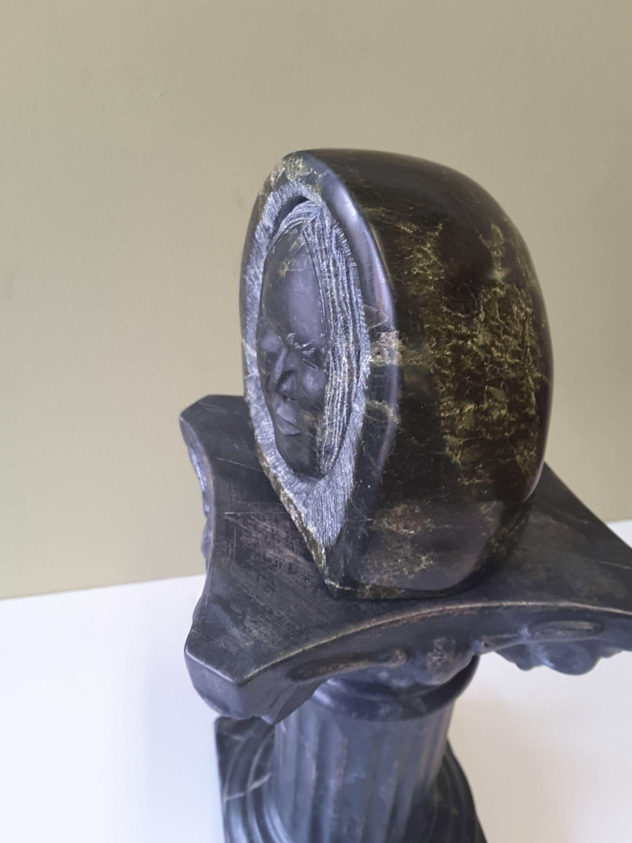 Sculpture inuit en stéatite représentant un visage enveloppé dans une capuche de parka. La tête est sculptée, de sorte qu'elle semble être mobile ou séparée de la capuche de parka. Le visage est bien détaillé et les yeux sont très bien faits. La