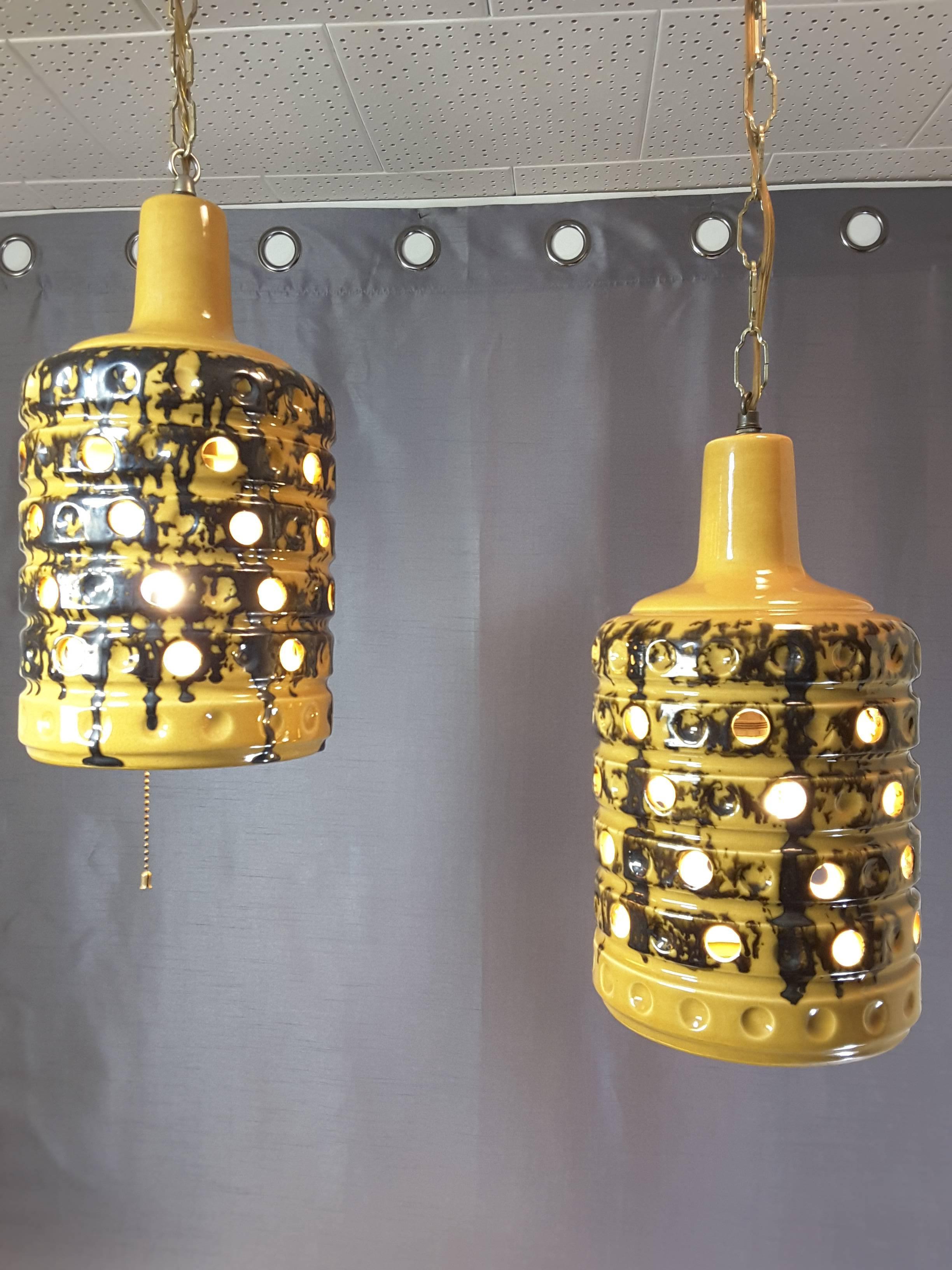 A pair of Mid-Century ceramic swag pendant lights, circa 1960's, done in deep mustard yellow with an earth tone dark brown sponge and drip accent. The lamps are open on the bottom and have off set holes on the sides for light. The top is a raised