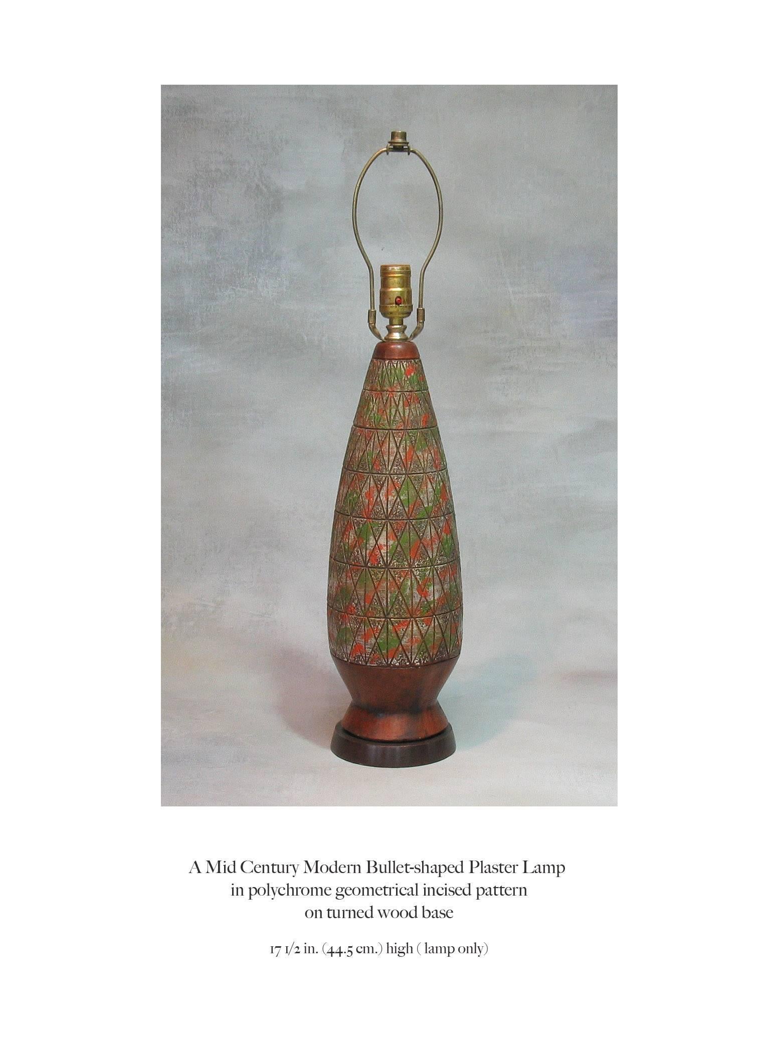 A Mid-Century Modern bullet shaped plaster lamp, in a polychrome geometrical incised pattern, mounted on a wood base. Burnt orange, green and silver grey colors. The lamp measures 17 1/2" inches high x 5" inches in diameter, circa 1960s.