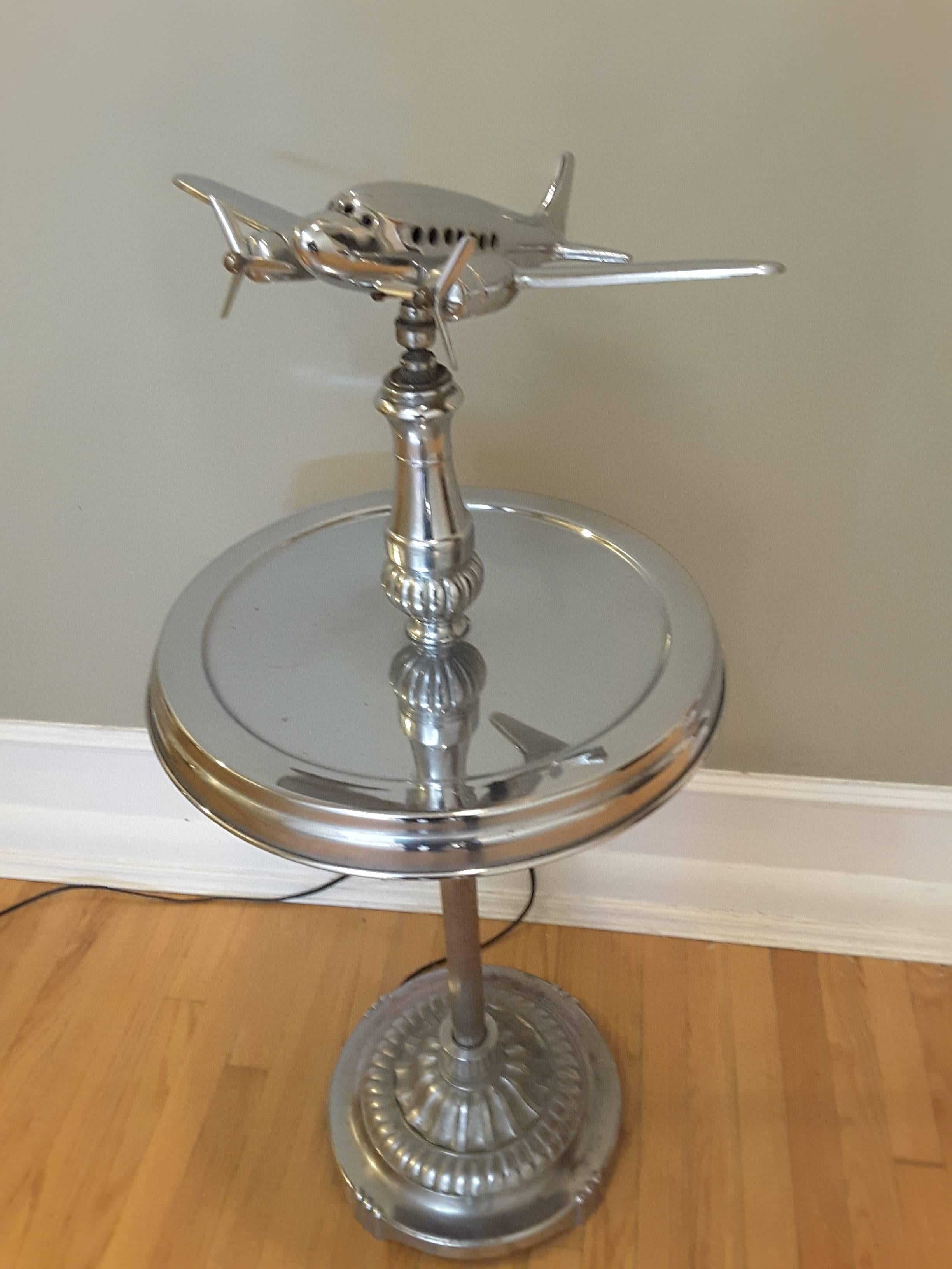 A Mid-Century chrome DC-3 airplane smoking table, light up interior cockpit and passenger section (switch is mounted under the airplane at the rear), twin propellers spin, the airplane swivels and tilts in any direction. The table section is for