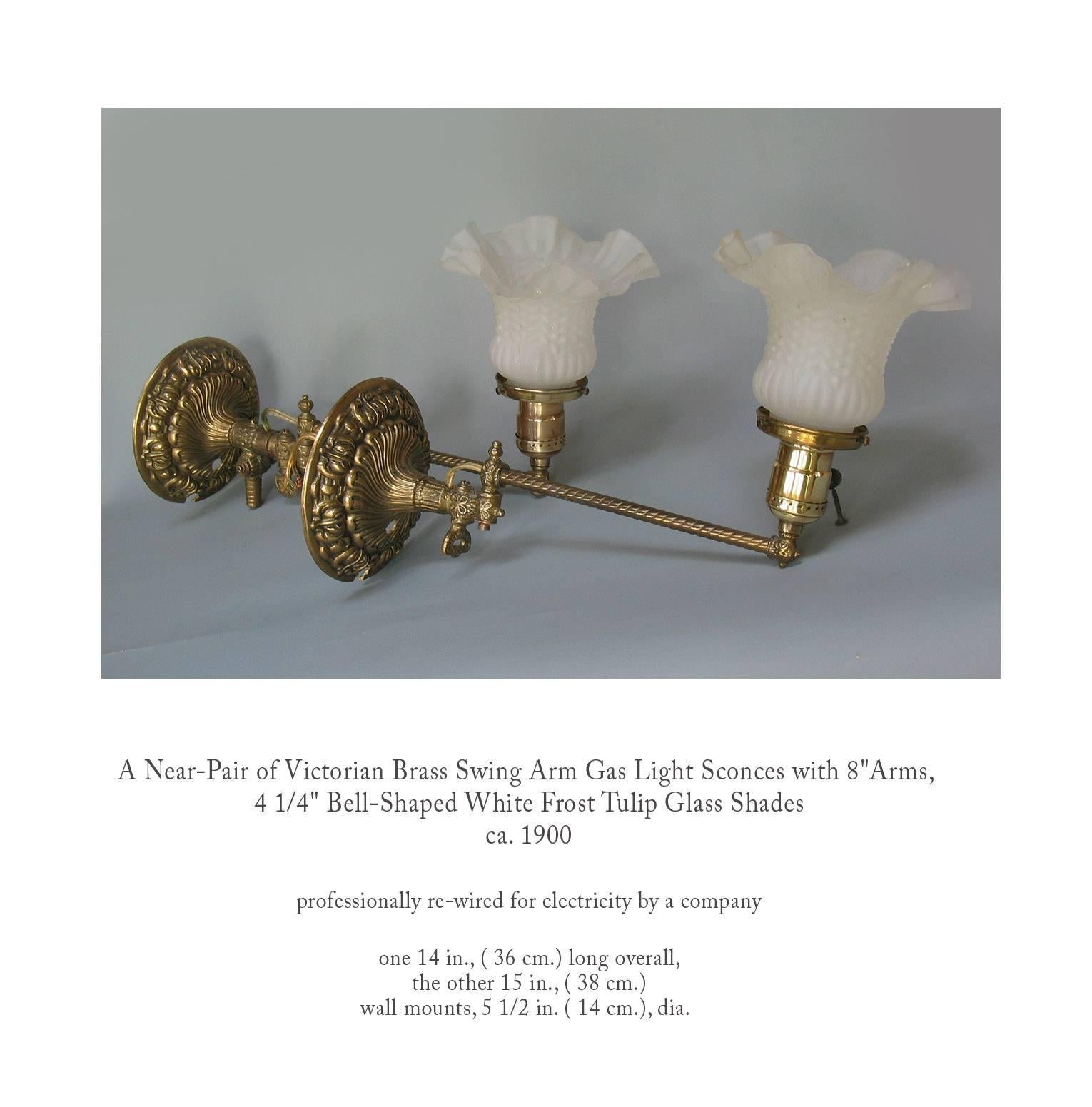 A near-pair of Victorian brass swing arm gas light sconces with 8"-inch arms, 4 1/4 " bell-shaped white frost tulip glass shades, circa 1900. Professionally re-wired for electricity by a company. One 14", (36 cm.) long overall, the