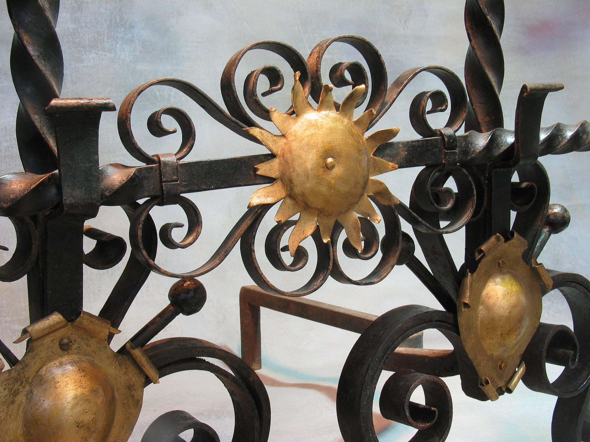 A pair of large Cannonball top wrought iron Andirons 19th century with cannonball tops on central twist stems supported by ornate scroll work feet with blind gilt metal crests, together with twist-turned cross bar ending with a ball on turned ends