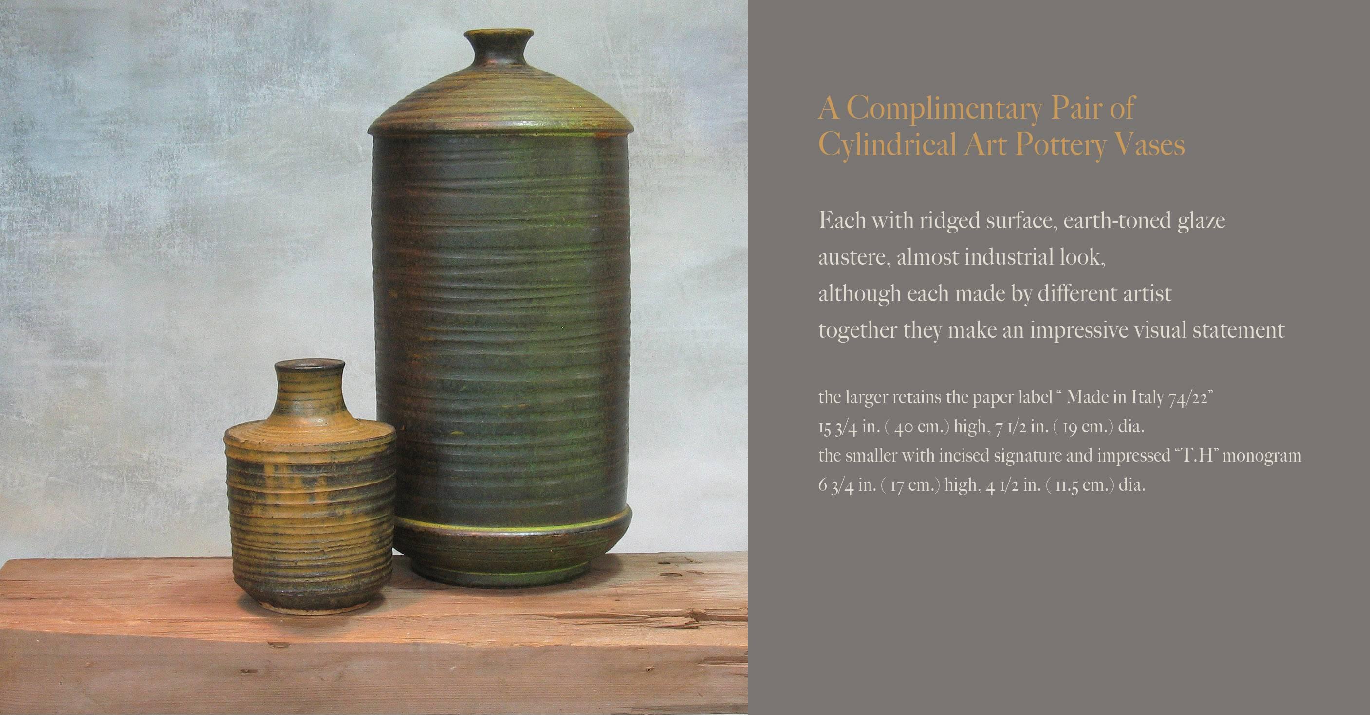 A complimentary pair of cylindrical art pottery vases, Each with ridged surface, earth-toned glaze austere, almost industrial look, although each made by different artists, together they make an impressive visual statement. The larger retains the