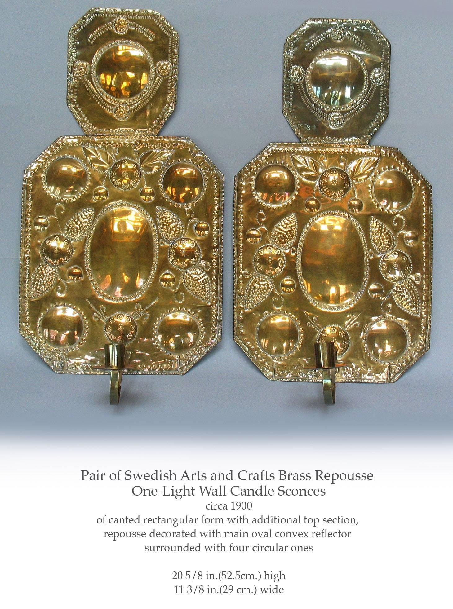 Pair of Swedish Arts & Crafts brass repoussé one light wall candle sconces, circa 1900, Of a canted rectangular form with additional top section, repoussé decorated with main oval convex reflector, surrounded with four smaller circular ones. The