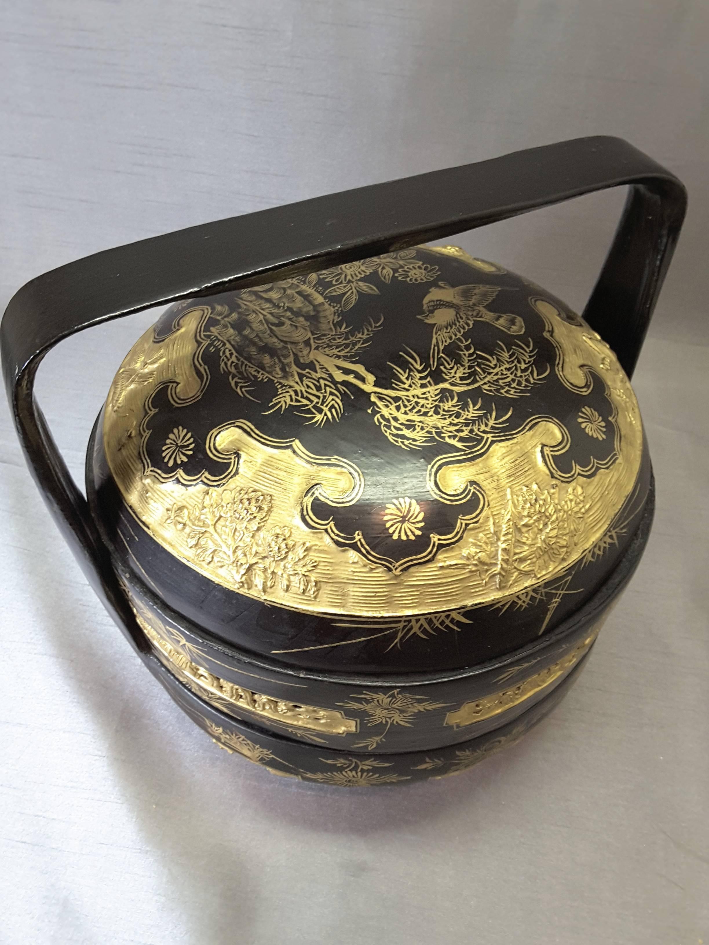 Chinese black lacquered and gilt food carrier/storage box, the box has a base with a center removable tray and lid. The handle is fixed to the base and is decorated with birds and floral motifs. The lid is done in the same manner and has a raised