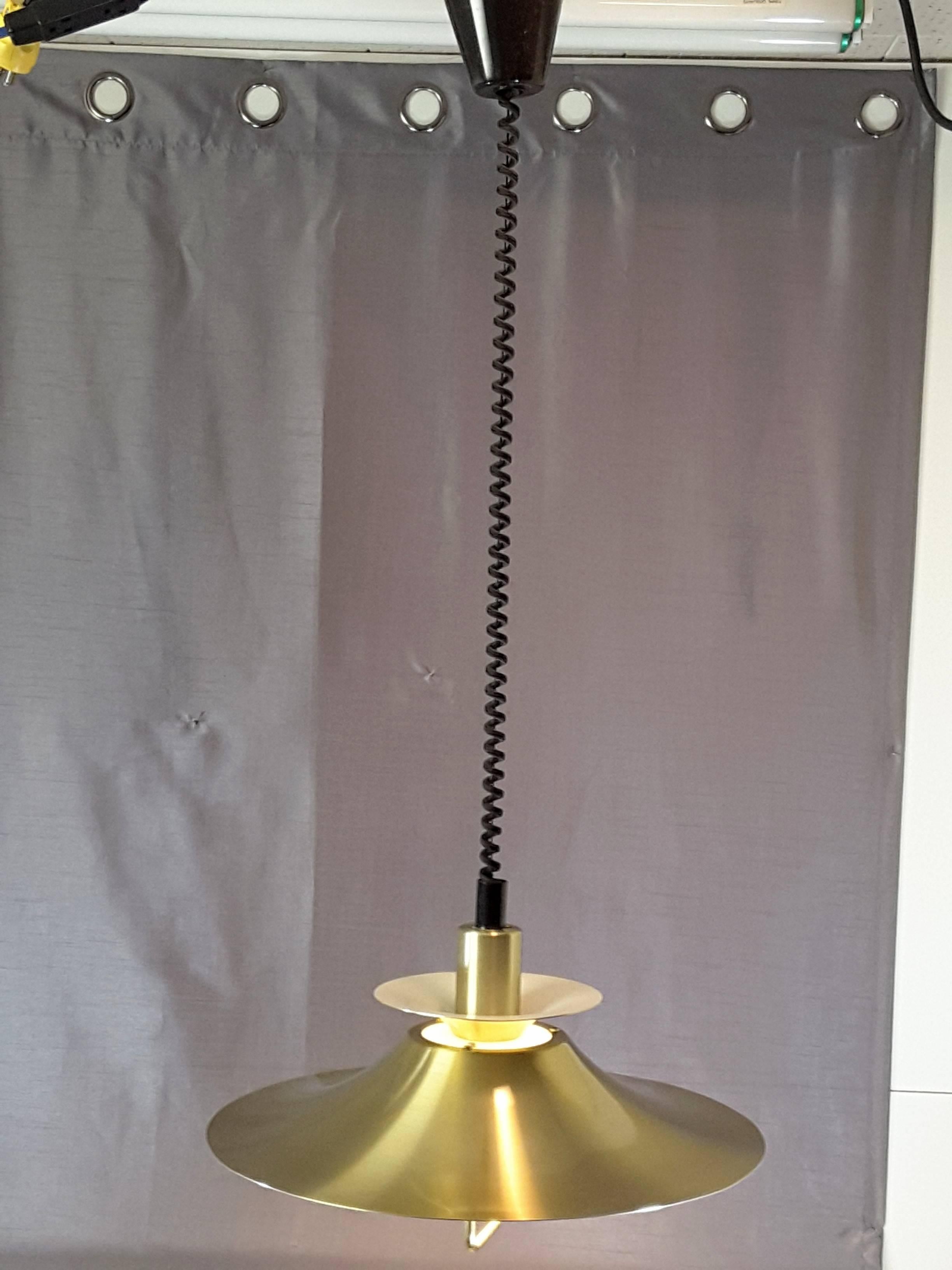 Frandsen retractable brass pendant, made in Denmark. The pendant is brass exterior, white interior, four ring, with a bottom pull-down brass handle. The fixture has a coiled wire, and easily retracts up and down. The fixture hangs 28