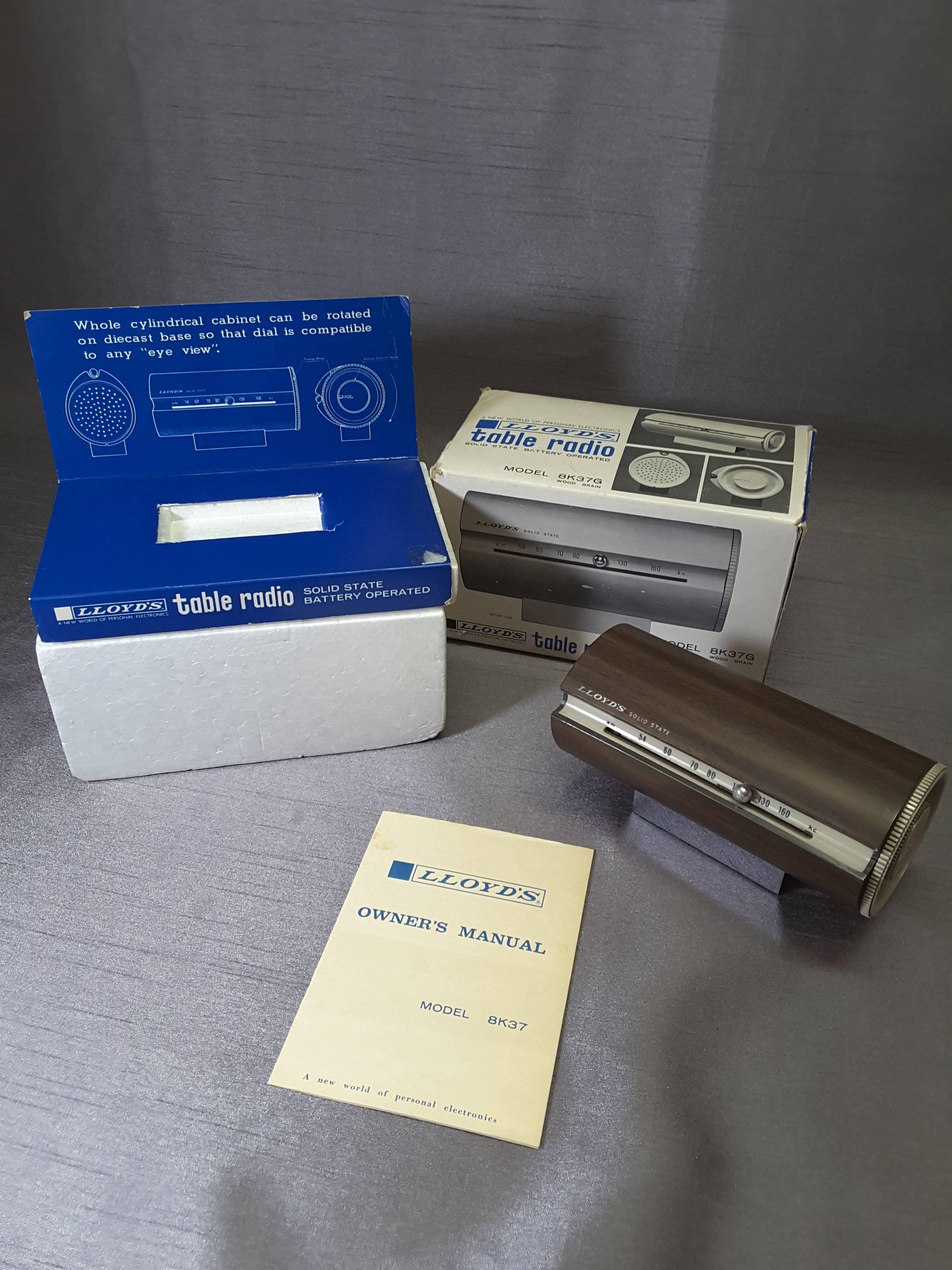 Mid-Century Modern 1967 wood grain finish tubular solid state am radio, desk or table radio In the Original box, packaging, and instruction booklet. Model 8K37G, mounted on a chrome base, the radio will rotate to keep the dial at eye level. The dial