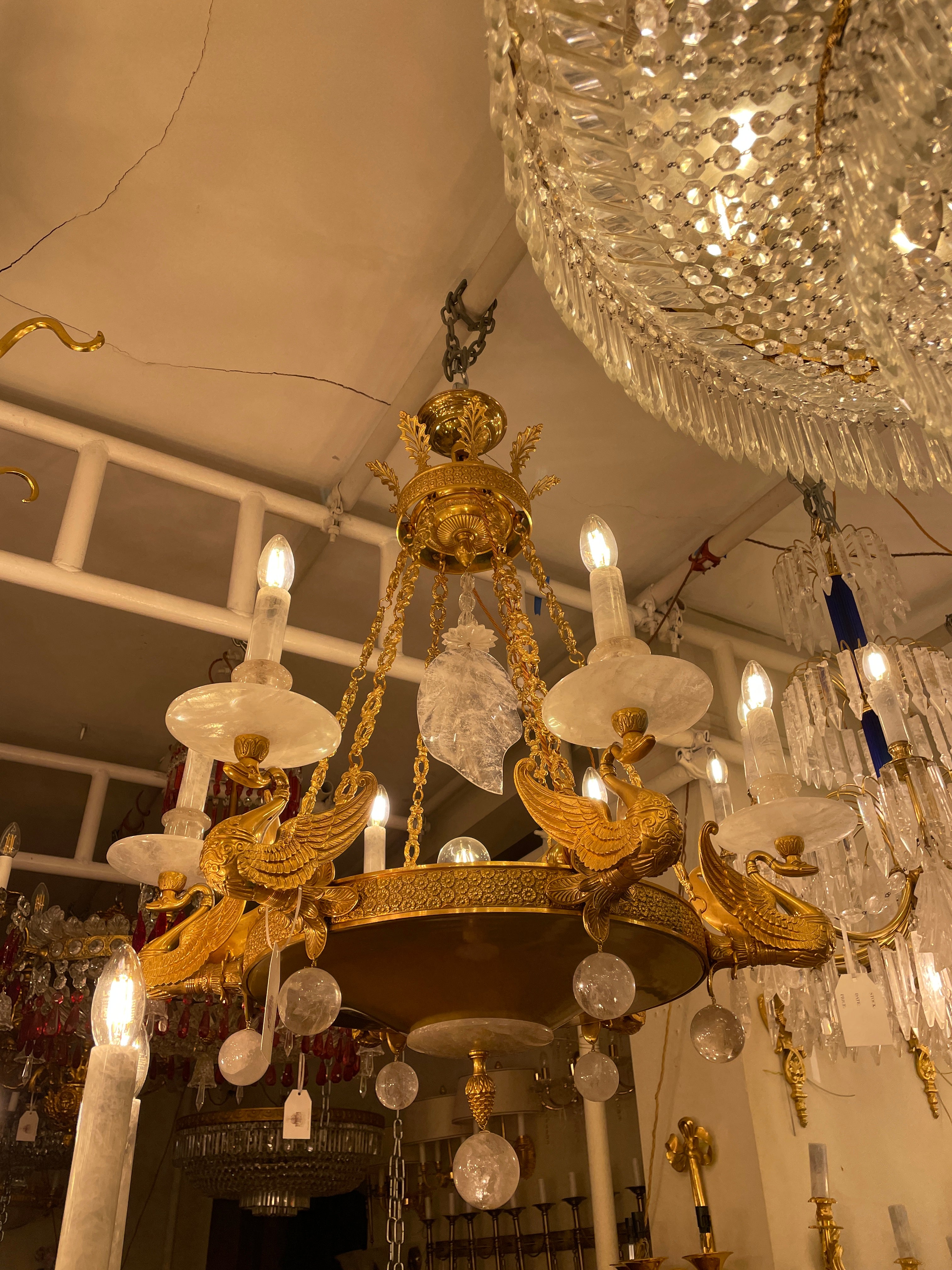 A beautiful gilded 10 light chandelier with 6 outer drip pans, nozzles and candle tubes all in rock crystal each surmounted on cast bronze swans of excellent quality. A central dish terminates with a small bronze decorated plate held in place by a