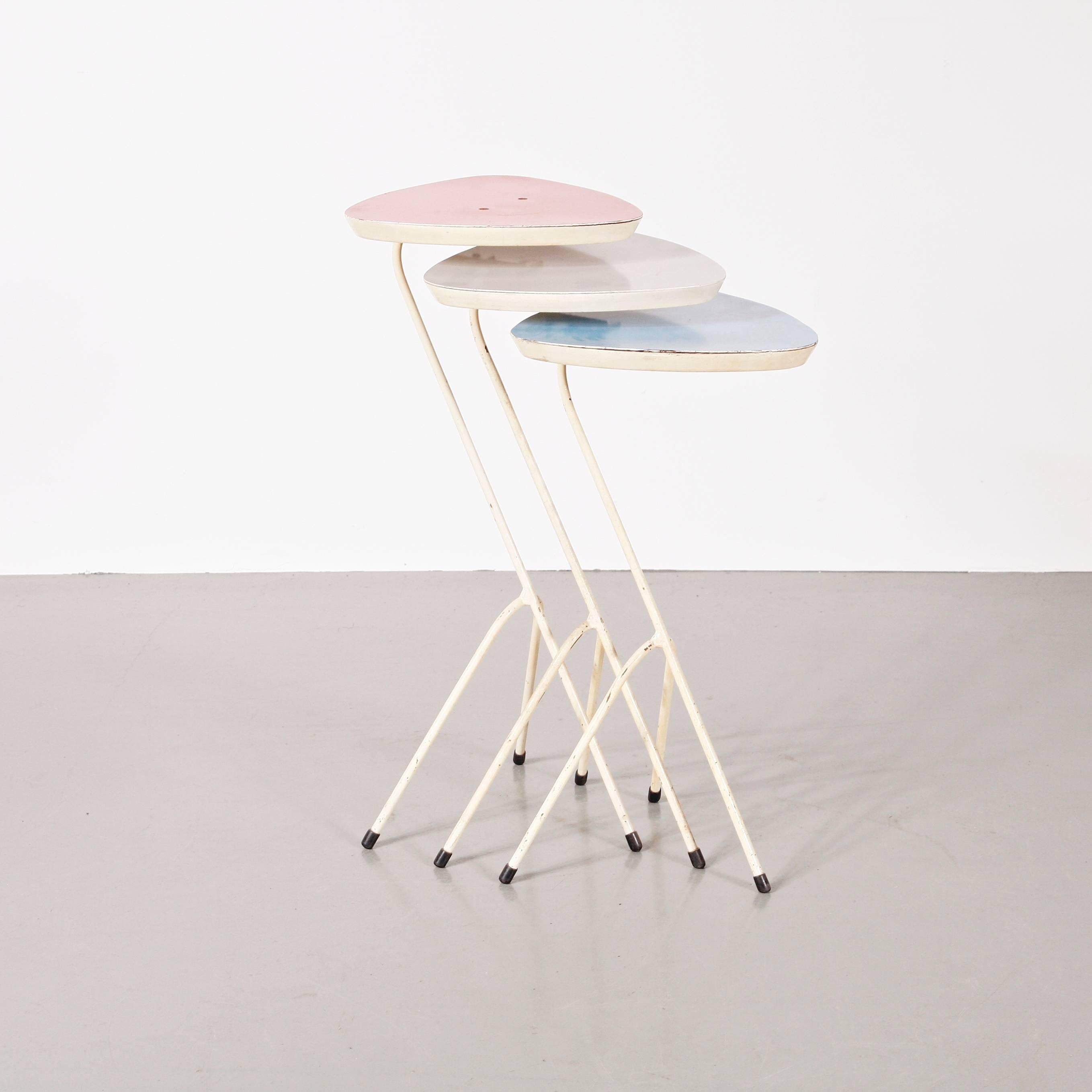 This vintage set of three formica-topped nesting tables was designed during the 1950s by Coen de Vries and produced by Devo in the Netherlands. The tables feature lacquered steel frames, formica table tops in blue, pink and grey. One of the table