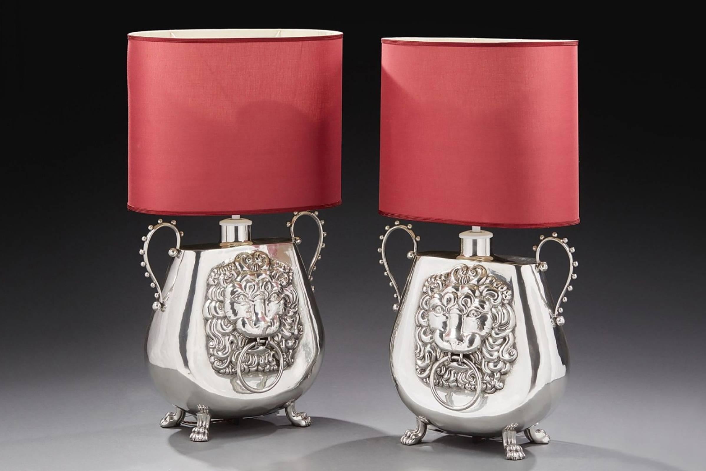 Lamp vase set of two with tin handles and four 
ornate claw feet. Each faces with embossed lion heads.
Vase: L 52 x H 51 cm.
Vase with shade: H 99 cm.
Unit price: 3450,00€.

 