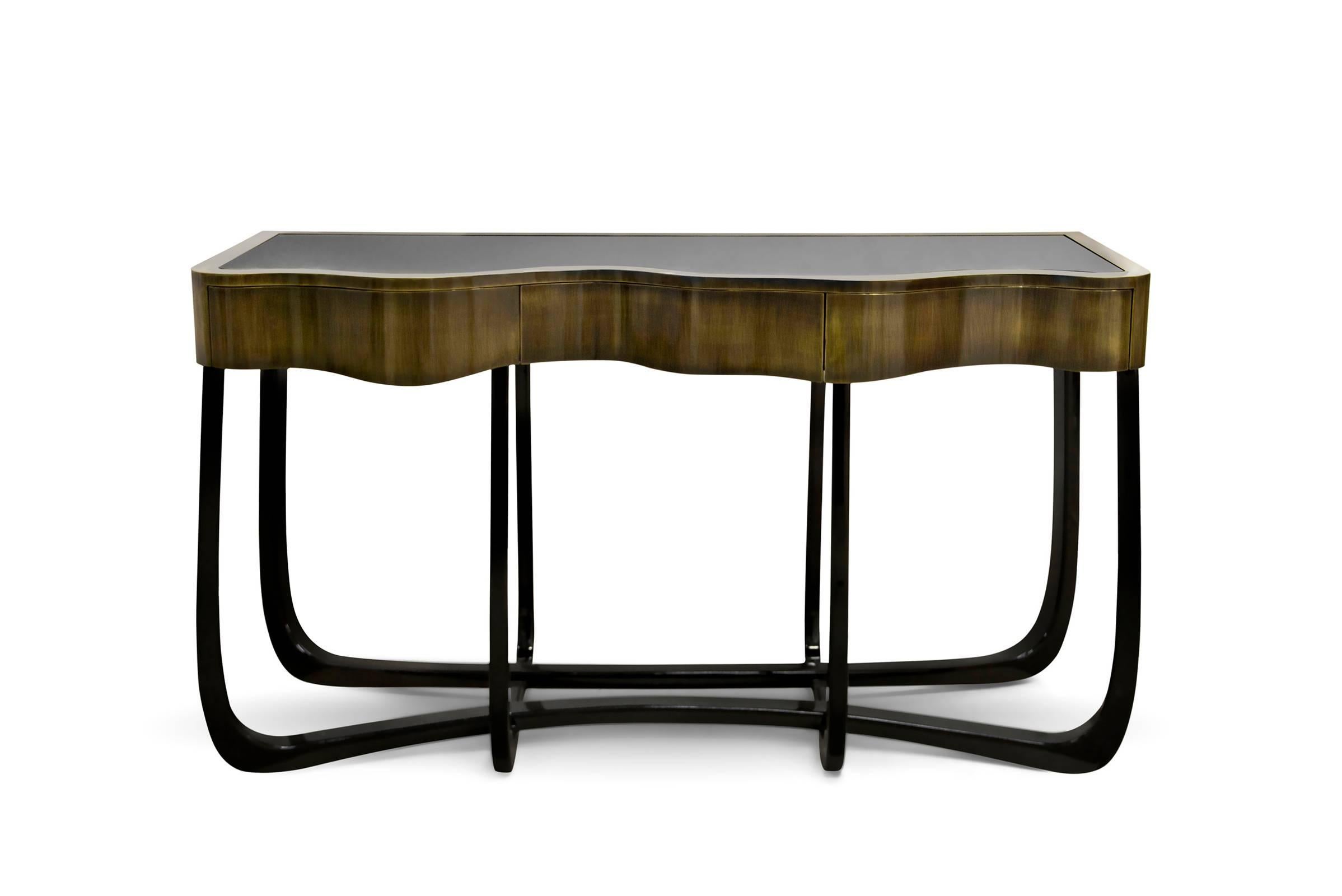 Table console Curvy avec structure supérieure en laiton patiné et avec des 
dessus plat en verre. Avec des pieds en acajou en finition laquée noire.
Disponible également en finition laiton poli doré ou en finition cuivre,
avec des pieds en acajou