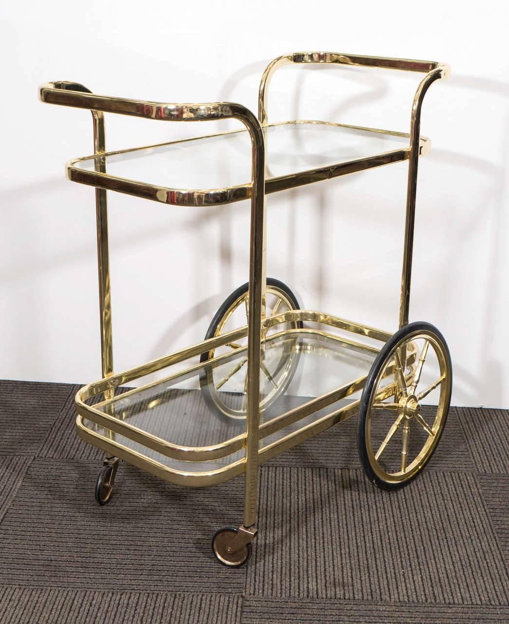 A stunning two-tier tea or bar cart in brass with spoke wheels in the style of Milo Baughman, circa 1970.