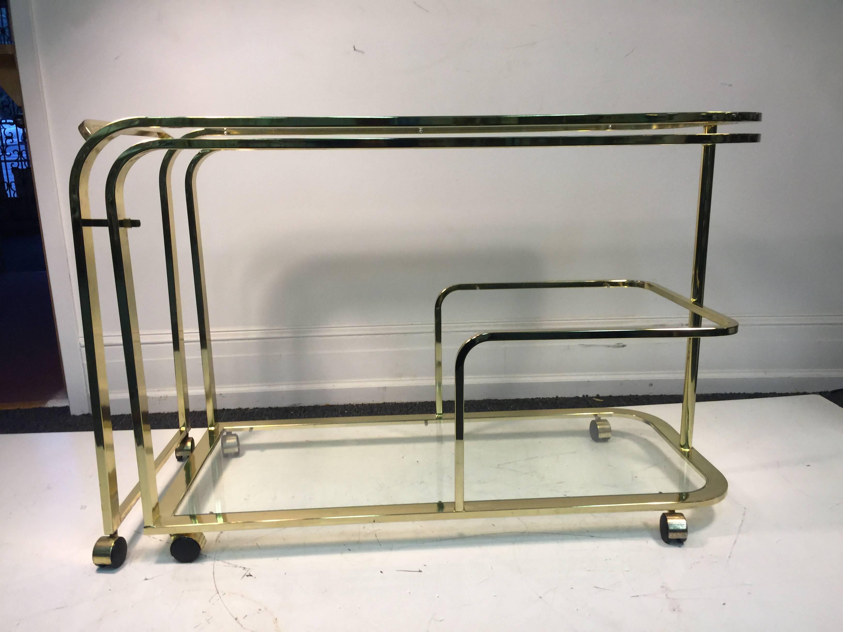 An exceptional, expandable, brass and glass bar or tea cart by Milo Baughman for design institute of America, circa 1970. Double the space for serving.