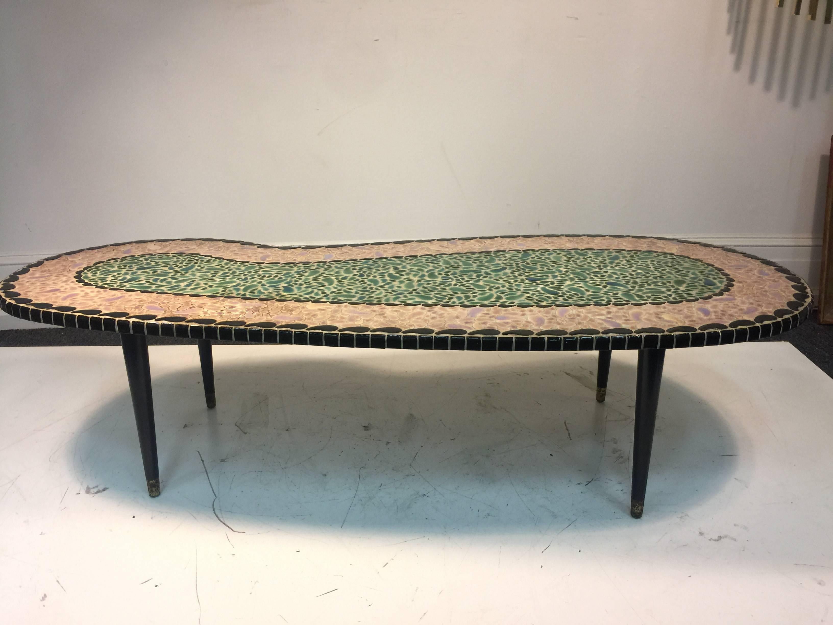 A magnificent mosaic tile top coffee table with beautiful colors, unusual kidney or boomerang shape and tapered legs with brass accent caps, circa 1970.