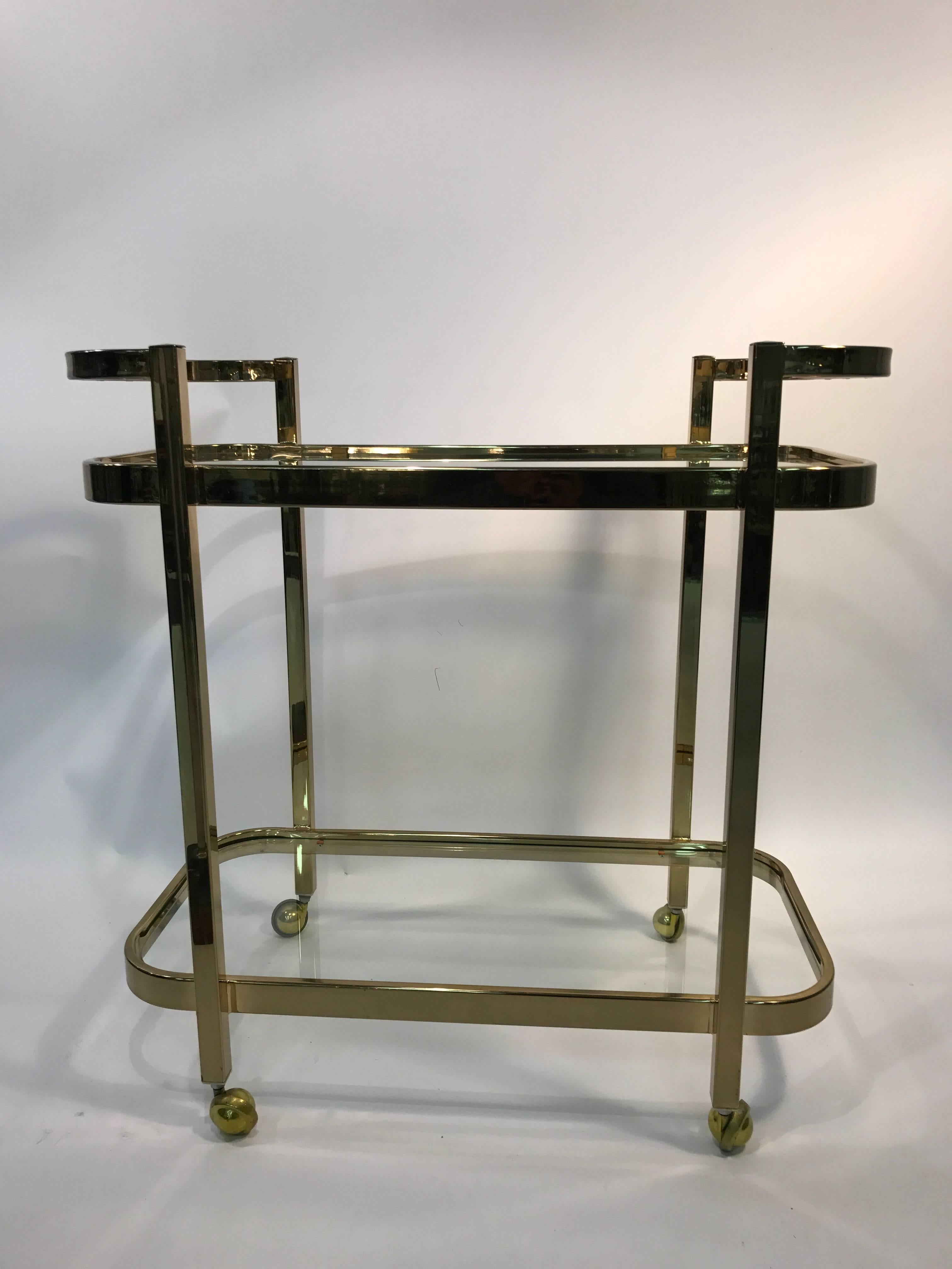 A beautiful two-tier brass and glass bar cart by Milo Baughman, circa 1970. Good vintage condition with age appropriate wear.