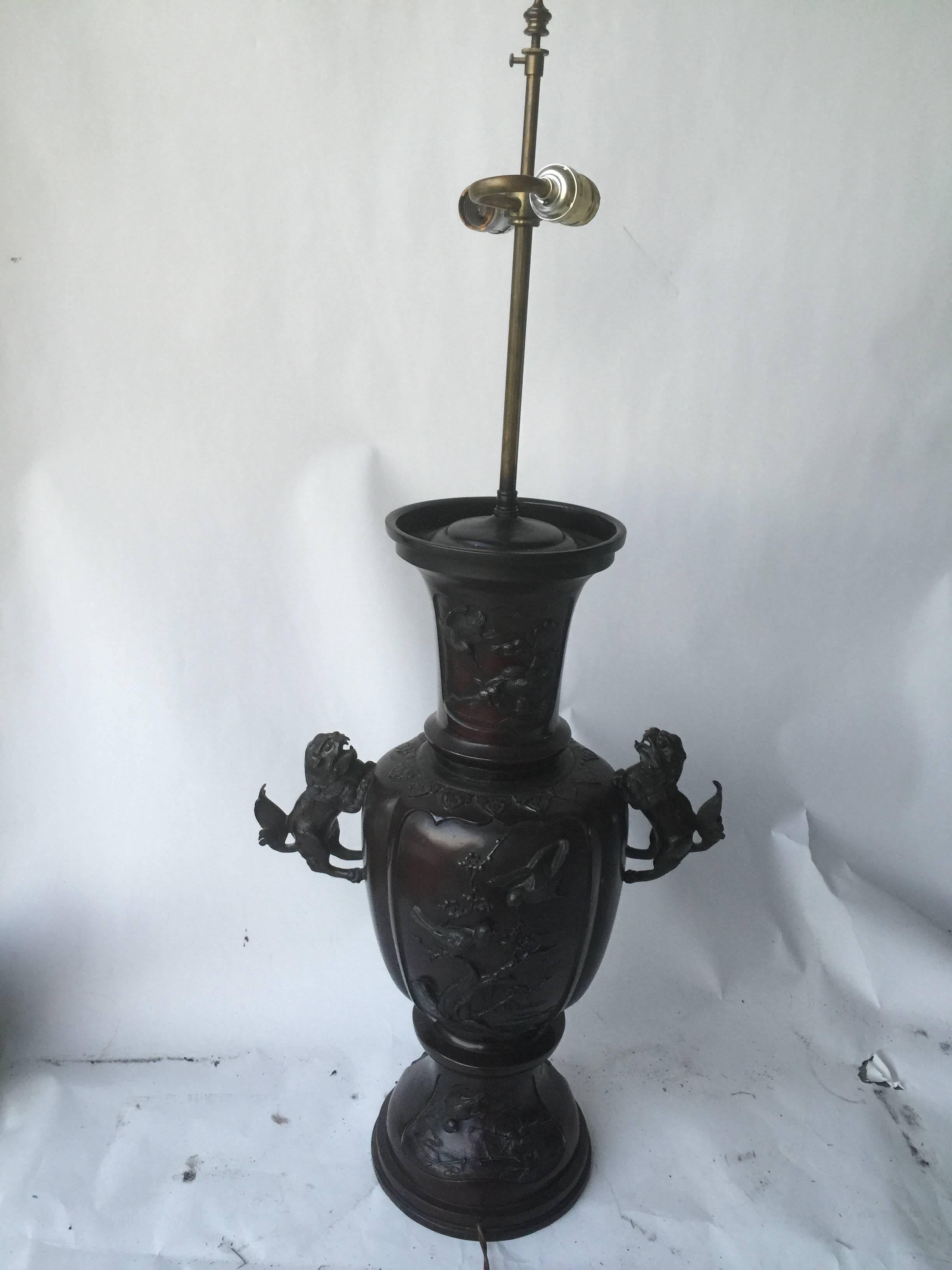 Pair of bronze Meiji period lamps highly decorated with foo dog handles and ornate birds on flowering branches in the center, top and base. Different exotic birds eating different berries amongst foliage. Each lamp has a double light fixture.