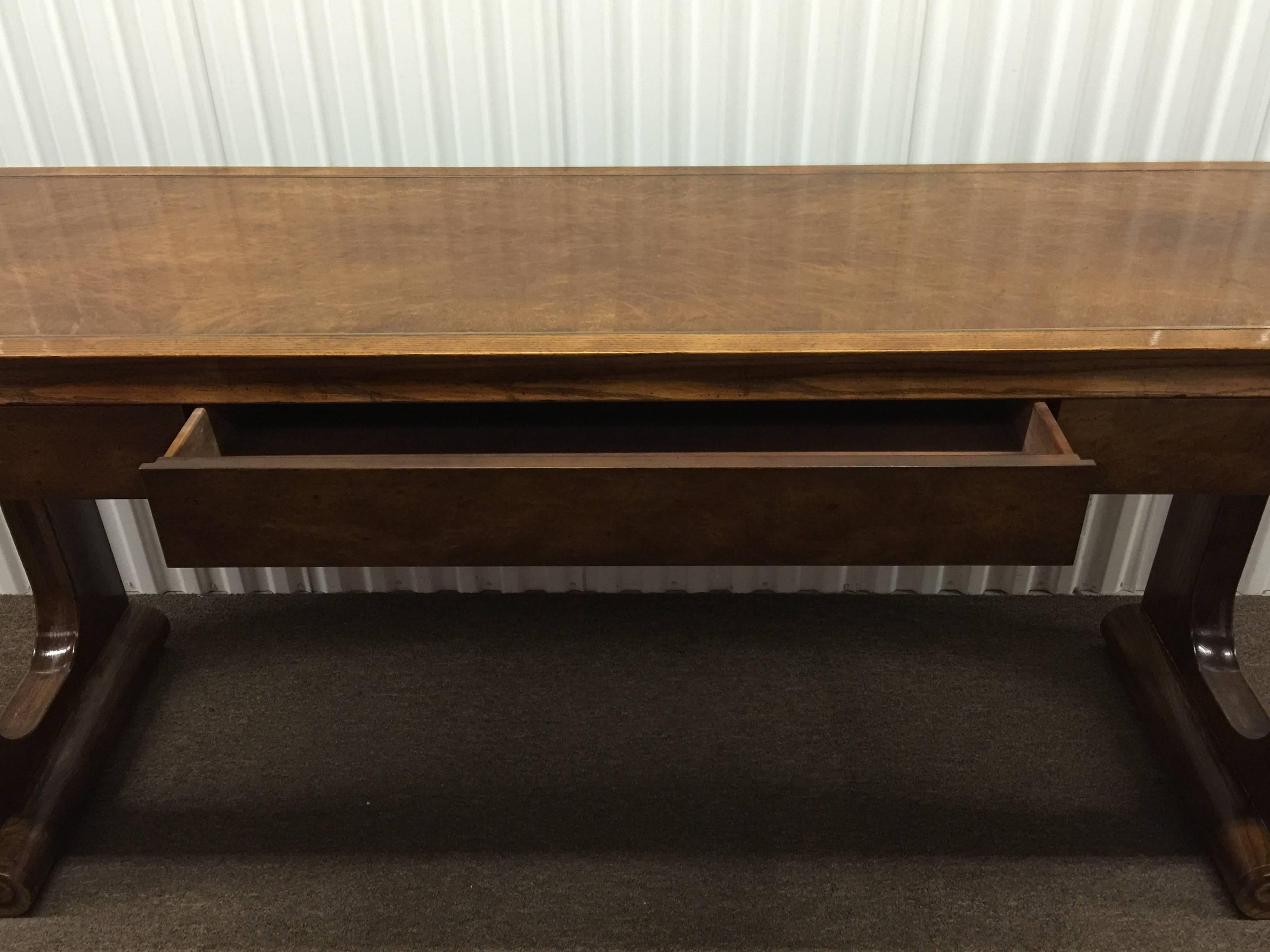 A great three-drawer console table inlaid with a Polished Brass Inlaid border on the top. Designed with scroll form legs and keyhole cutouts. This is a sturdy console made with burled oak. There is an area of some slight water damage in the right