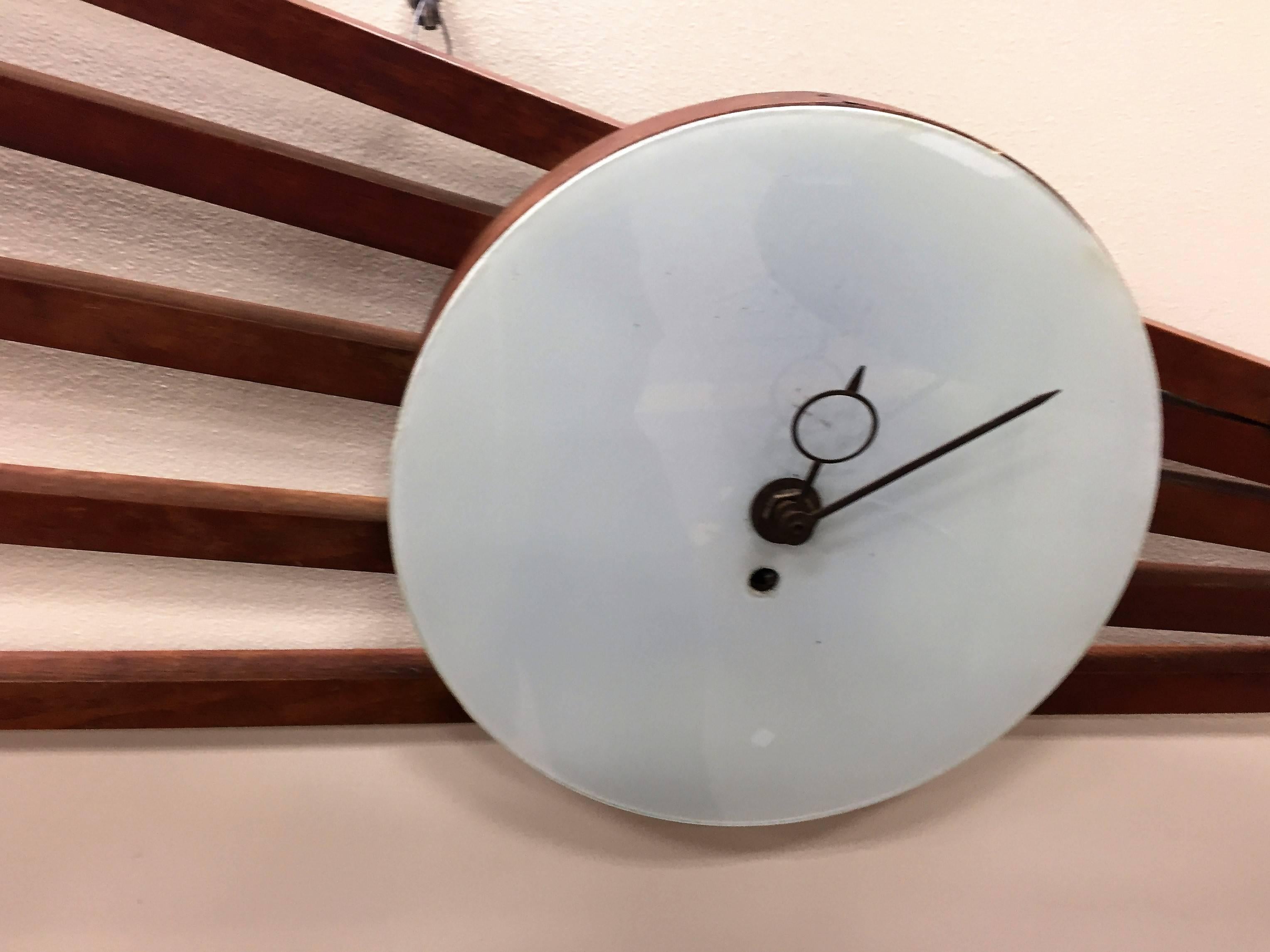 Comet like slatted wood and brass ball and stick wall clock with a key wind mechanism. Bright white enamel face. Great for a Mid-Century high end space,
for form and function alike.