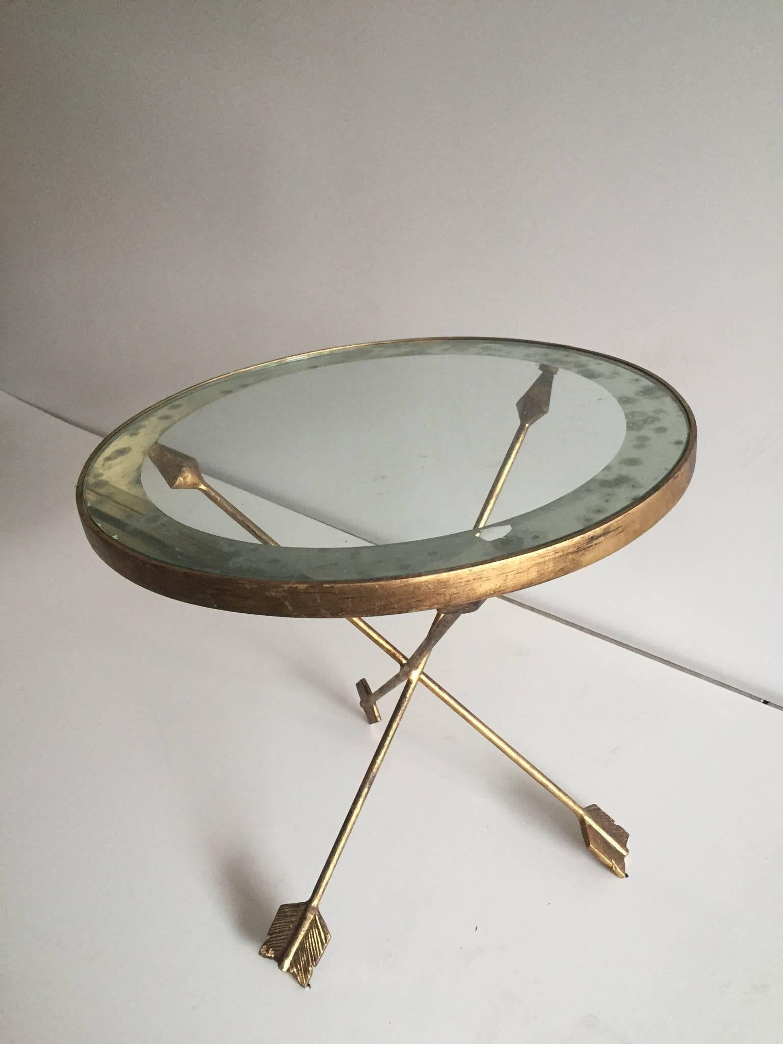 A French, brass end or side with arrow bases and circular glass top inspired by Maison Jansen.