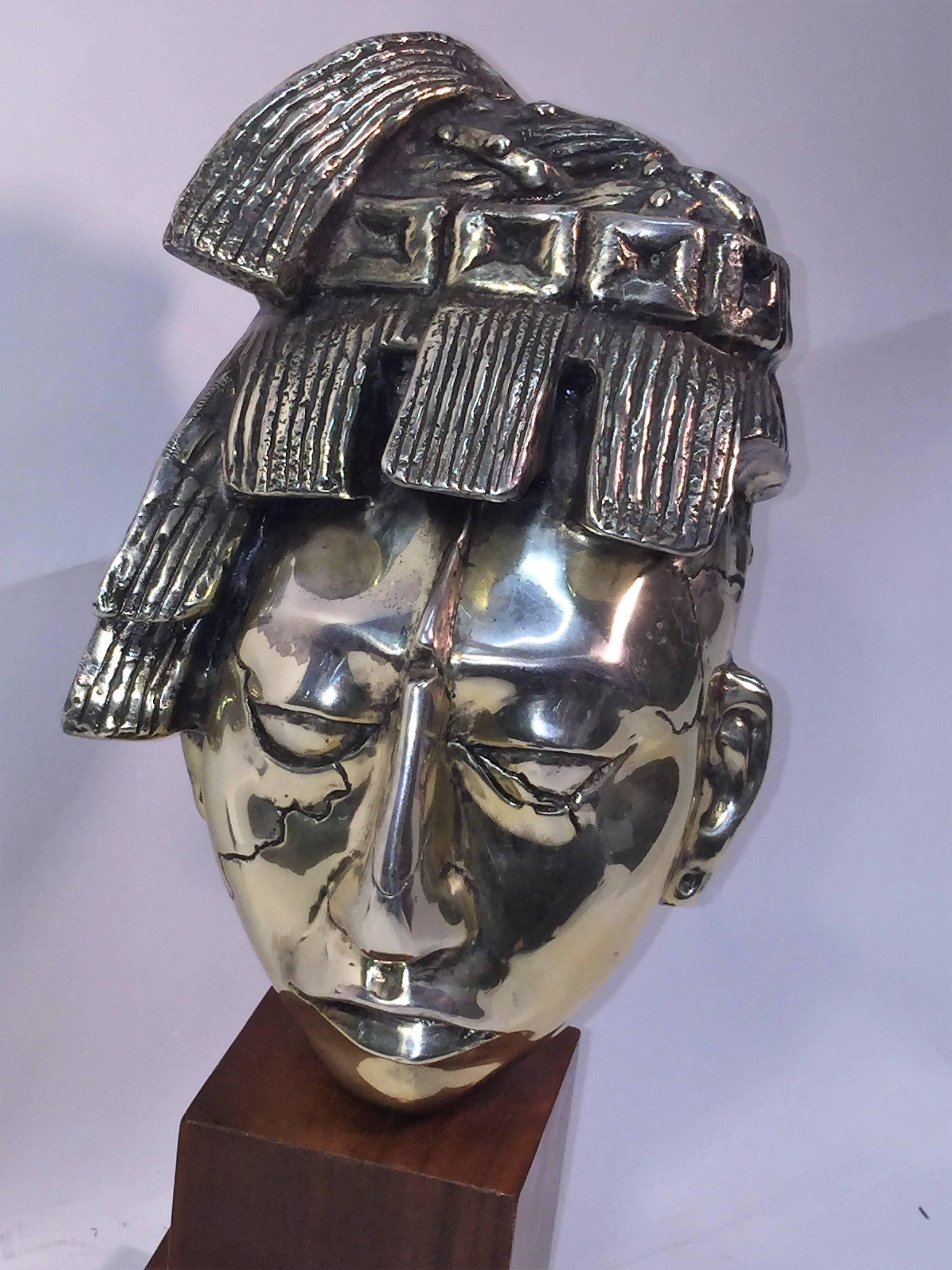 Modernist slivered bronze head of an Aztec warrior mounted on a quality wood pedestal, circa 1970s, cool sculpture for a console or grouping in a modern interior. The measurements of the wood base is 1' square and 1