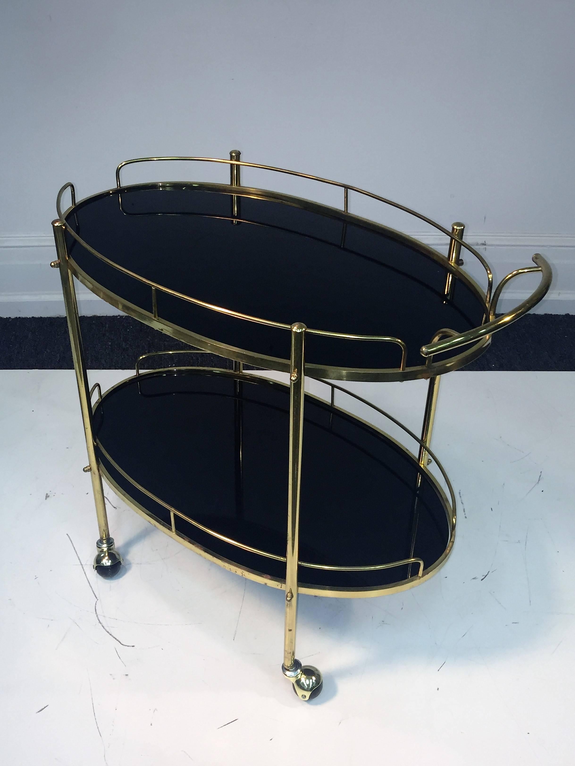 Great tubular brass modern bar cart with beautiful rare solid black glass oval shelves. Simple and elegant design suited for many interiors on black and brass caster wheels. The great quality oval black glass is removable for easier cleaning.