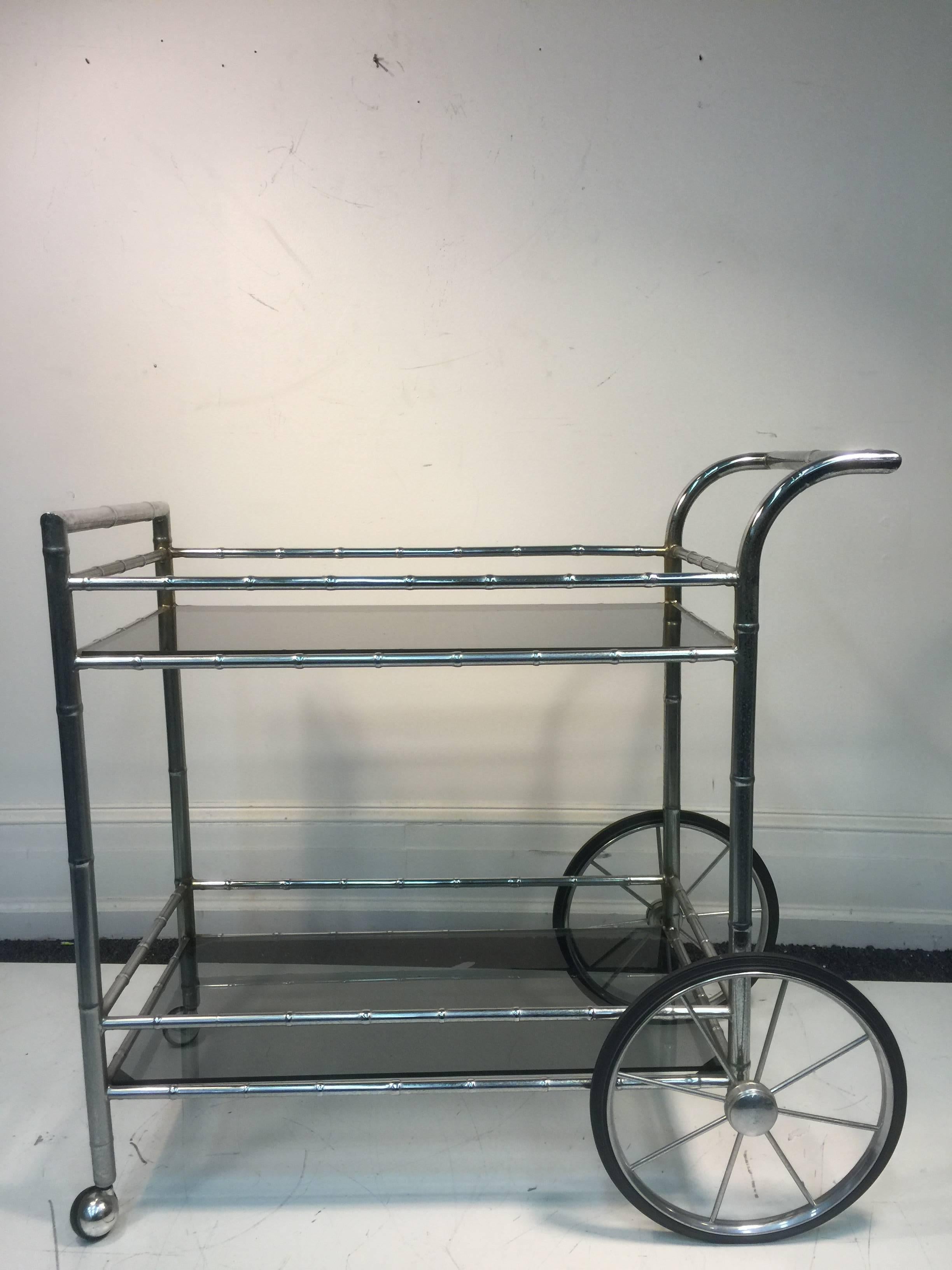 A striking two-tier faux bamboo chrome and smoke glass tea or bar cart, circa 1970. Good condition with age appropriate wear.