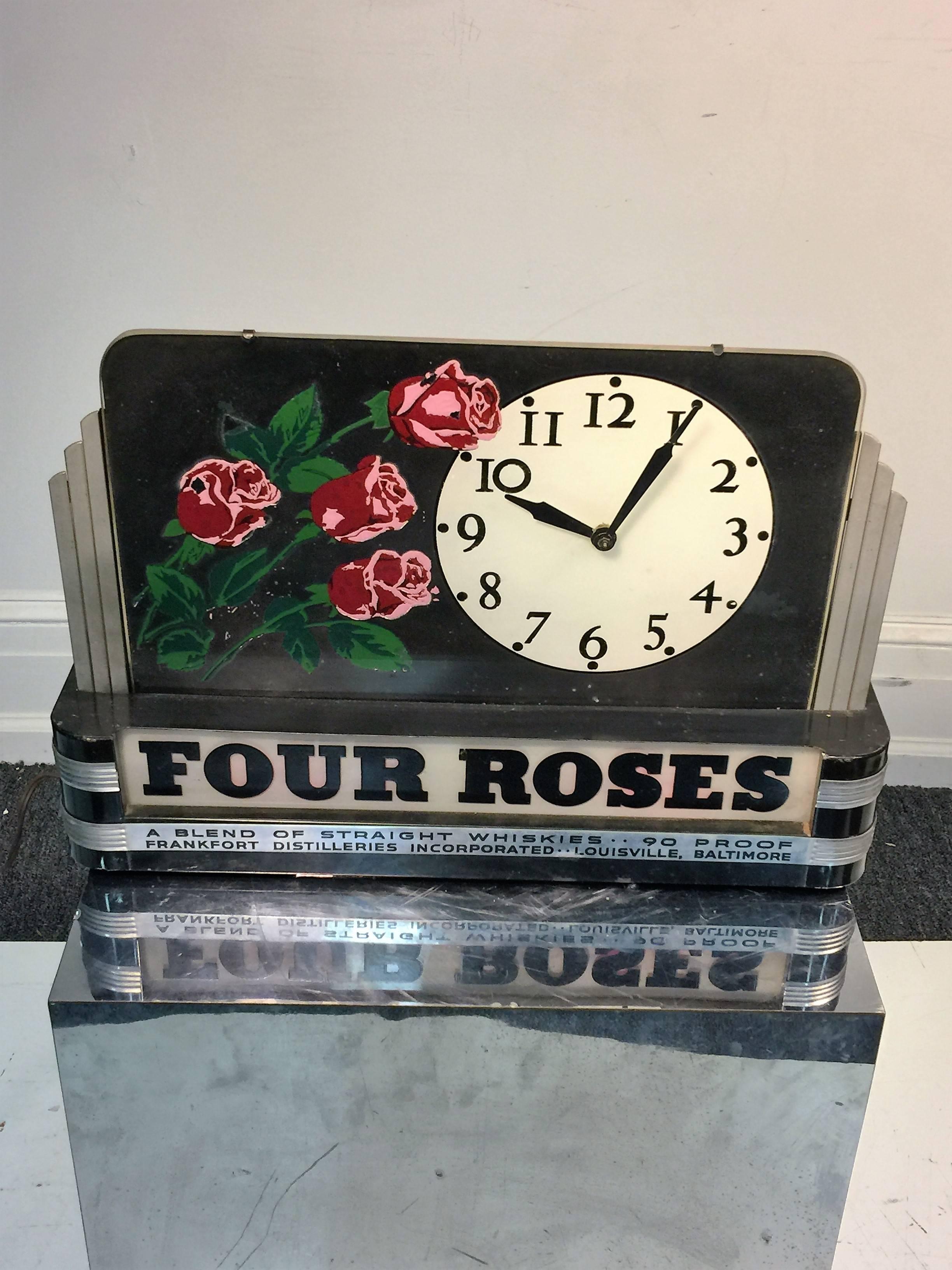 Period 1930s Art Deco black enameled metal and chrome stepped frame and double banded base reverse painted glass clock advertising four roses whiskies. When switch is turned on the base is lit from within and uplights the reverse painted clock face.