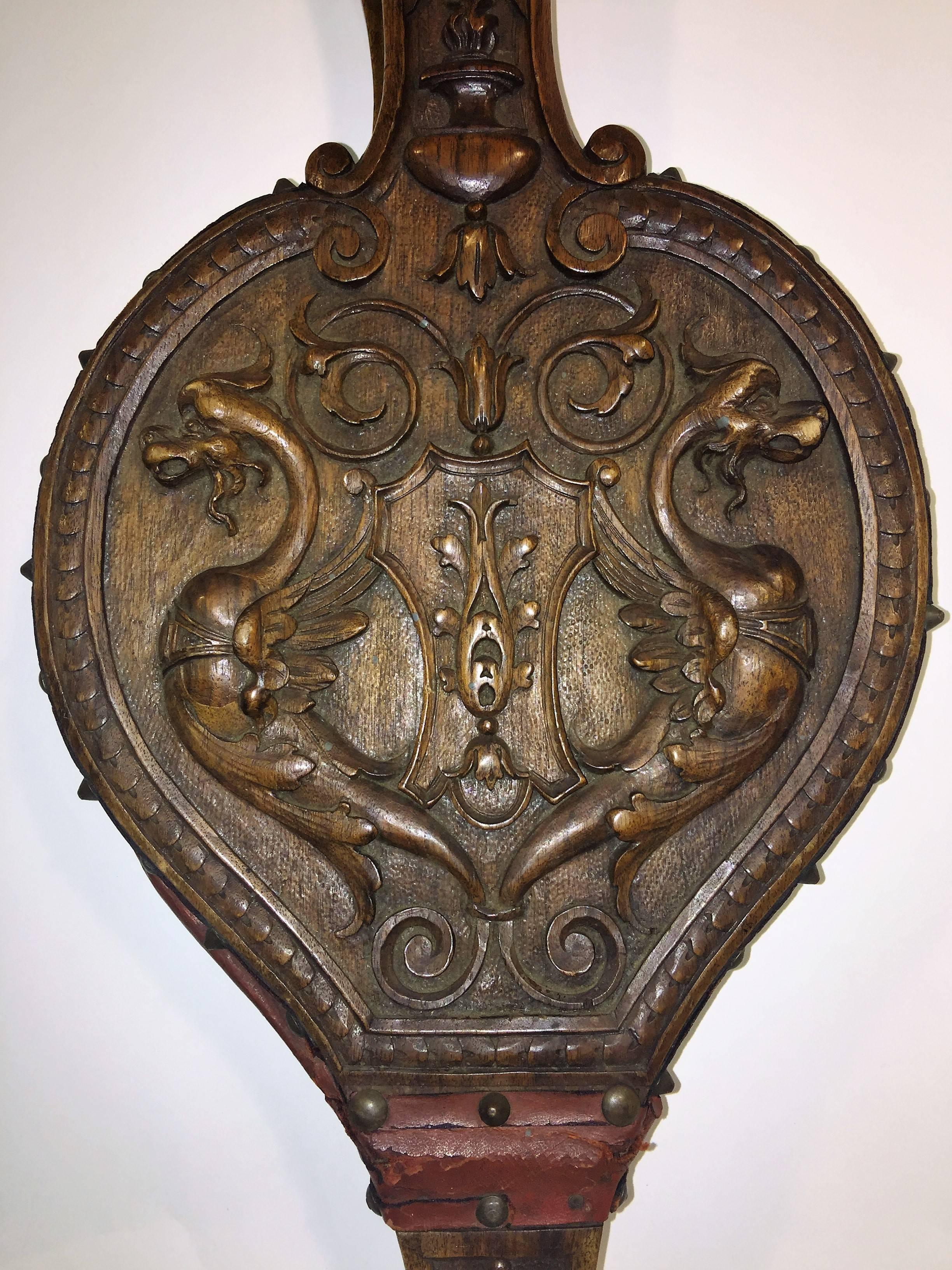 Intricately carved Italian fire bellows decorated with winged griffins, roaring lion head and torch and coat of arms and on the verso a beautiful carved north wind face. Lined with a red leather to expand the bellows to fan a fire. Studded with