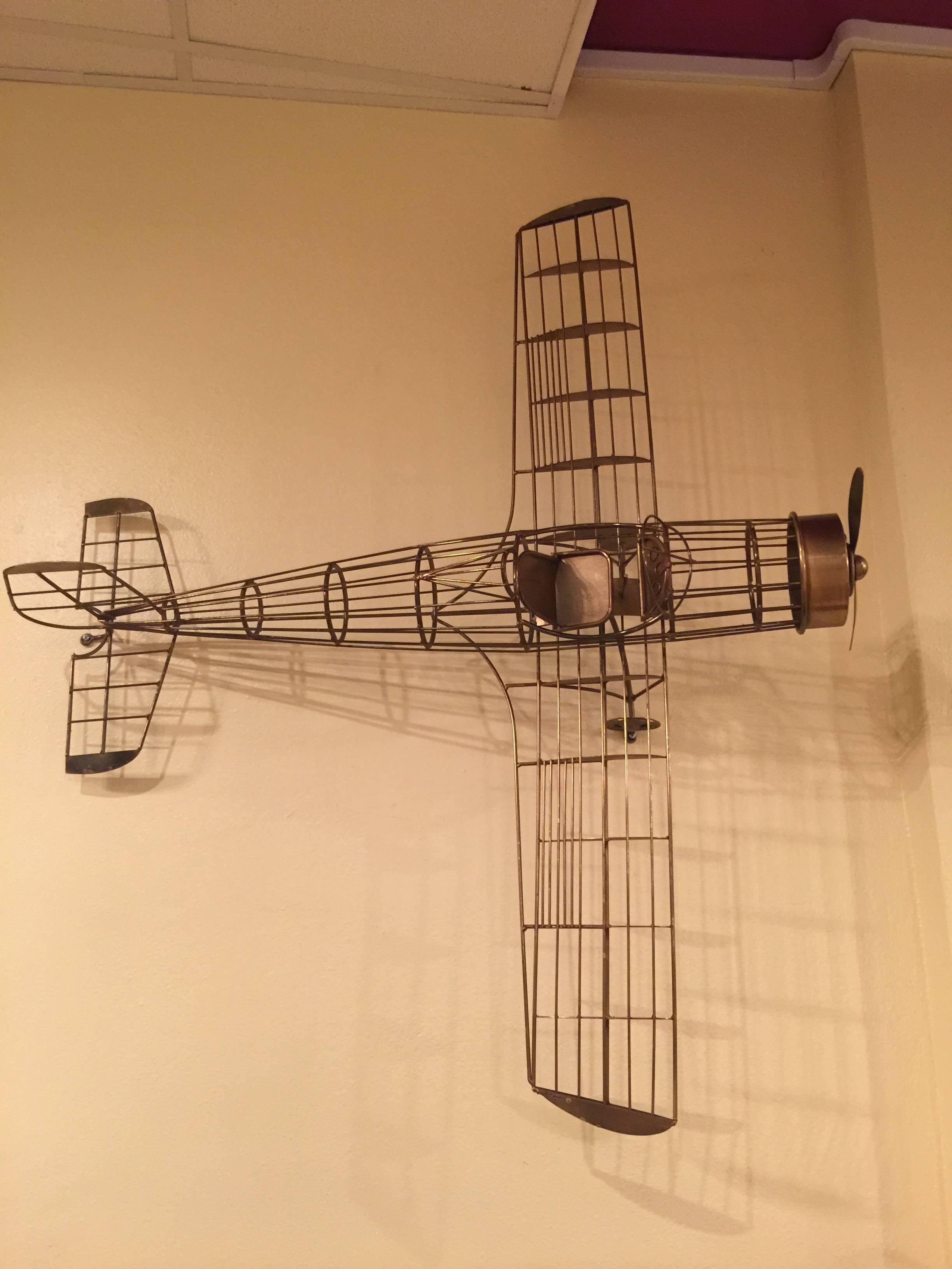 Gold tone sculpted three dimensional metal wire form airplane with propeller that spins. Great mounted on the wall or hung as a mobile from a decorative ring mounted from the ceiling.