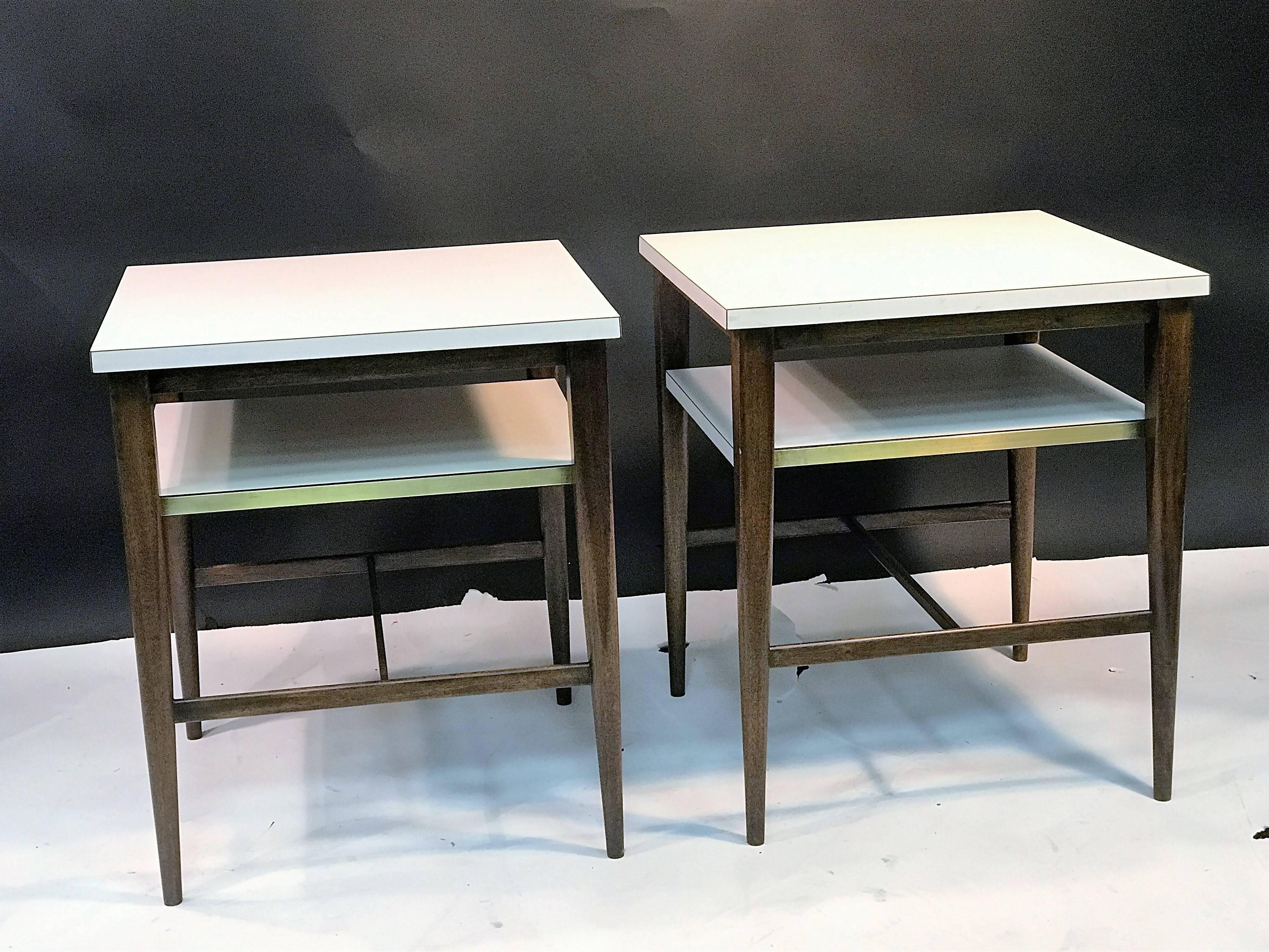 Fantastic high end pair of Paul McCobb double tier square top tables with a white laminate top and second laminate shelf that slides out on brass runners to accommodate cocktails, reading material etc. Beautiful walnut legs and stretchers complete