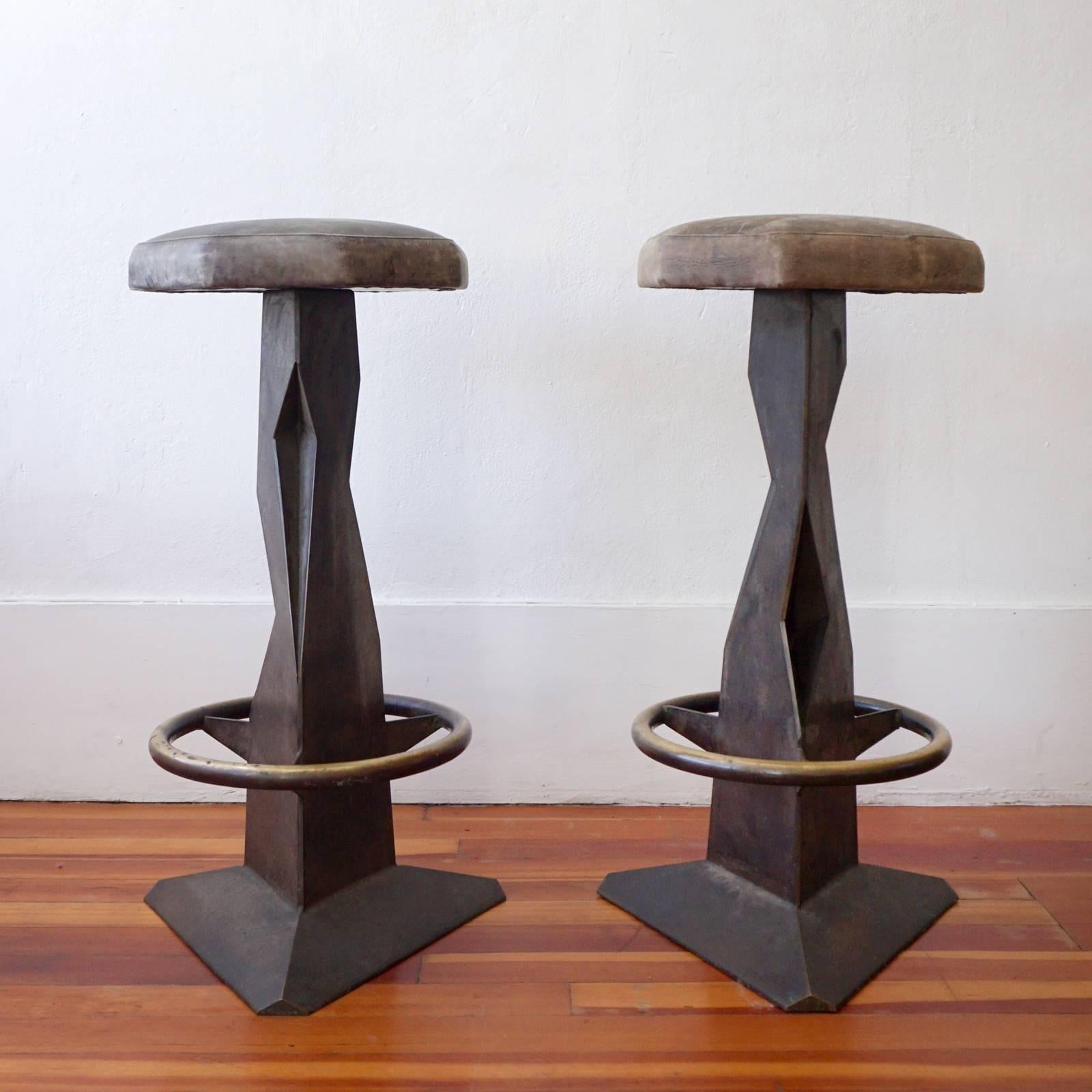 A pair of brutalist metal bar stools with a bronze finish and octagonal leather seats. High quality construction with a rich patina. The rotating seats are two different colors.