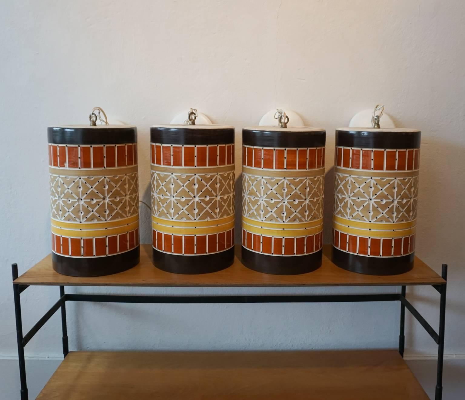 Set of four pierced ceramic hanging light fixtures. Orange, brown and yellow glazed cylinders with holes to allow for diffused light.