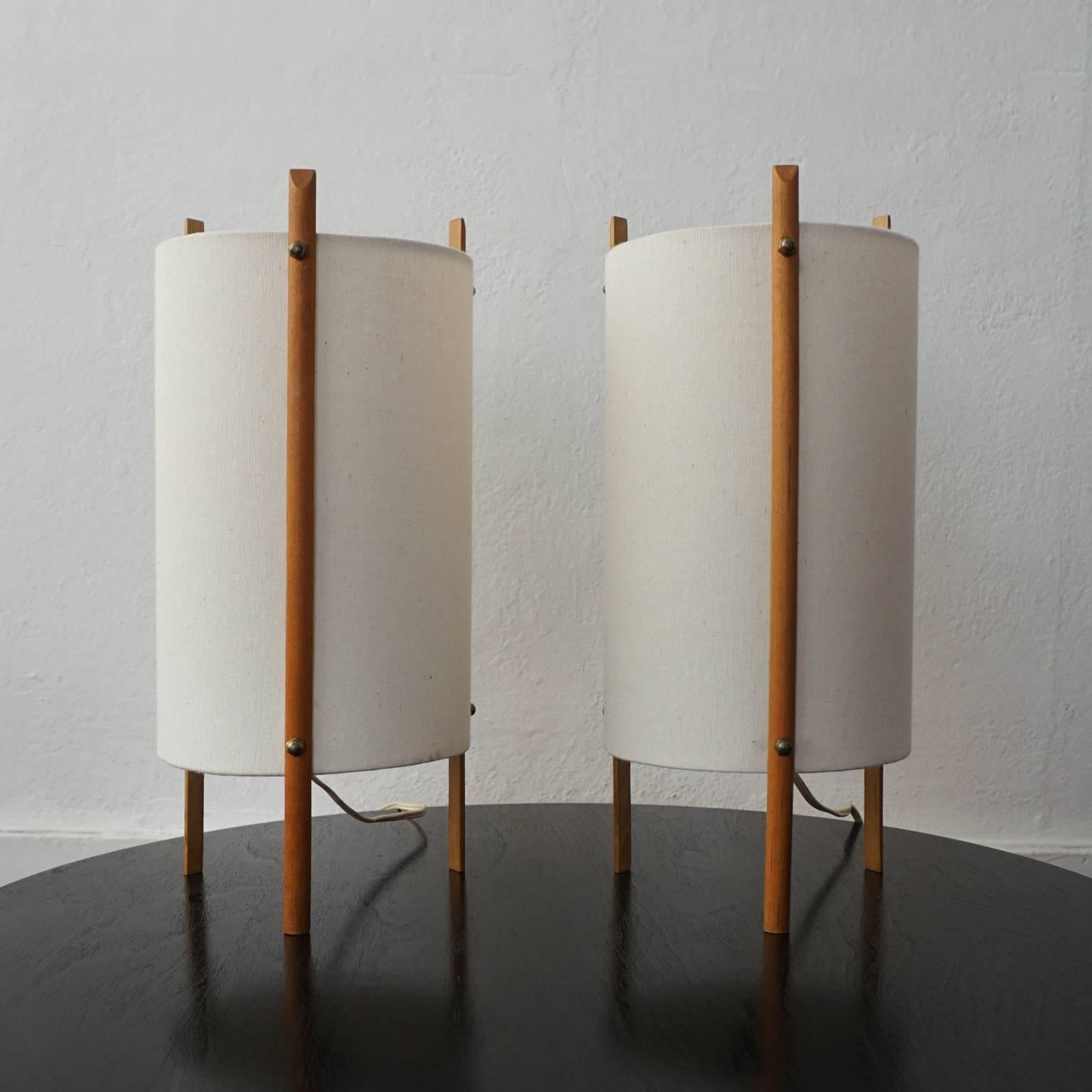 A pair of 1950s cylinder lamps. Teak tripod legs with brass fittings and natural linen shades. Made in Japan.