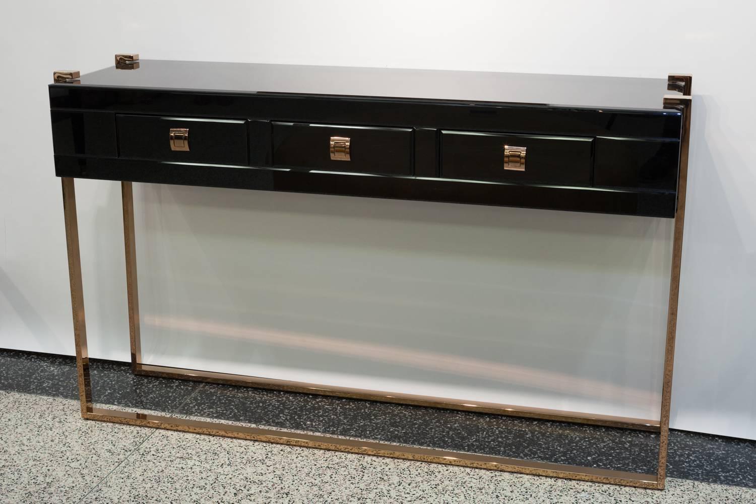 A stunning and dramatic black glass three-drawer console table with brass details and belt-buckle drawer pulls. The brass an elegant rose colored gold. 
In the Manner of Jacques Adnet 
