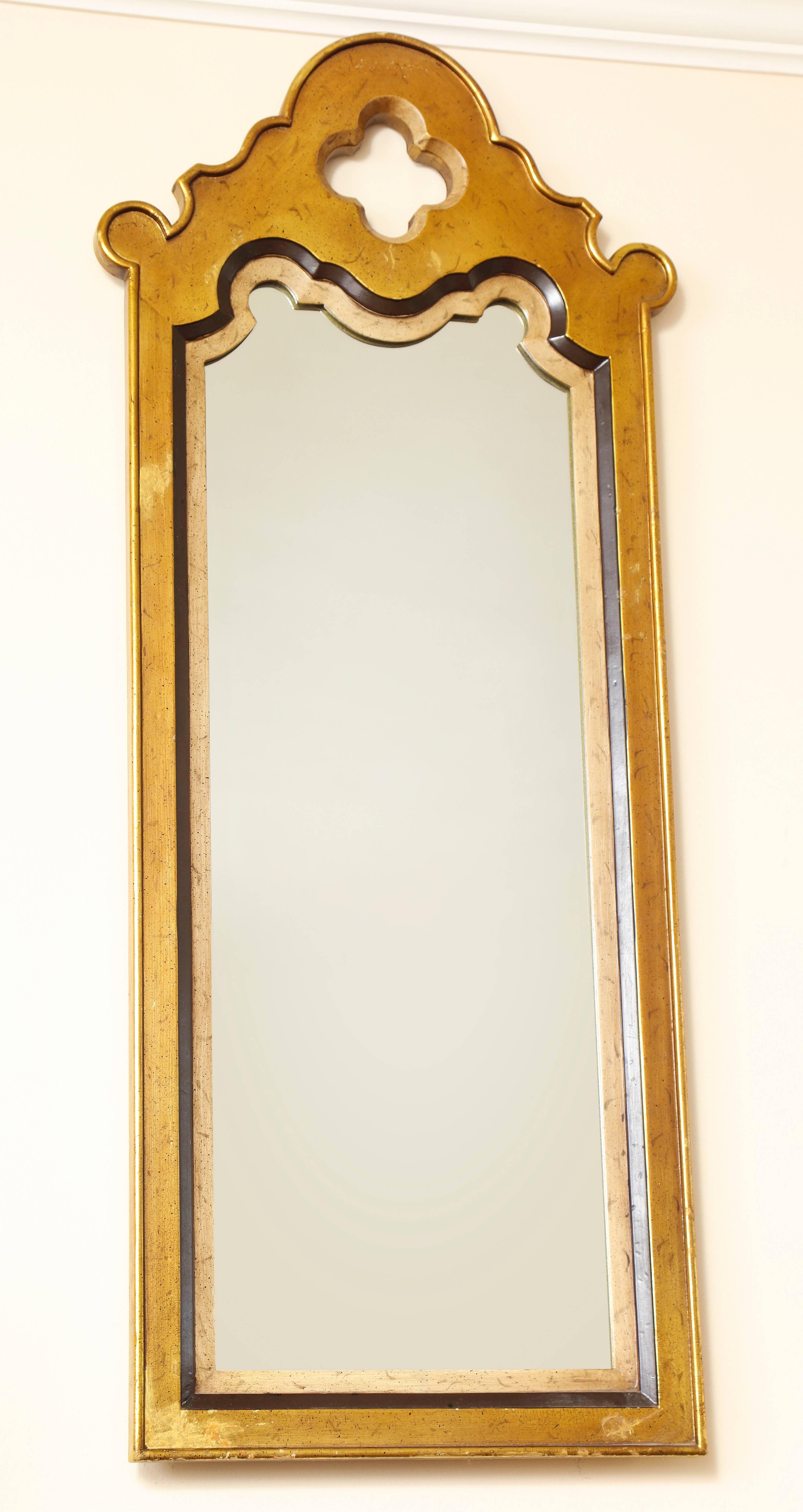 A striking Mid-Century Modern tall and narrow wall mirror with quatrefoil crown; having a Moorish design influence. Made by Drexel Heritage in the Hollywood Regency style with patinated gold and silver leaf finish. Original stamp on back with