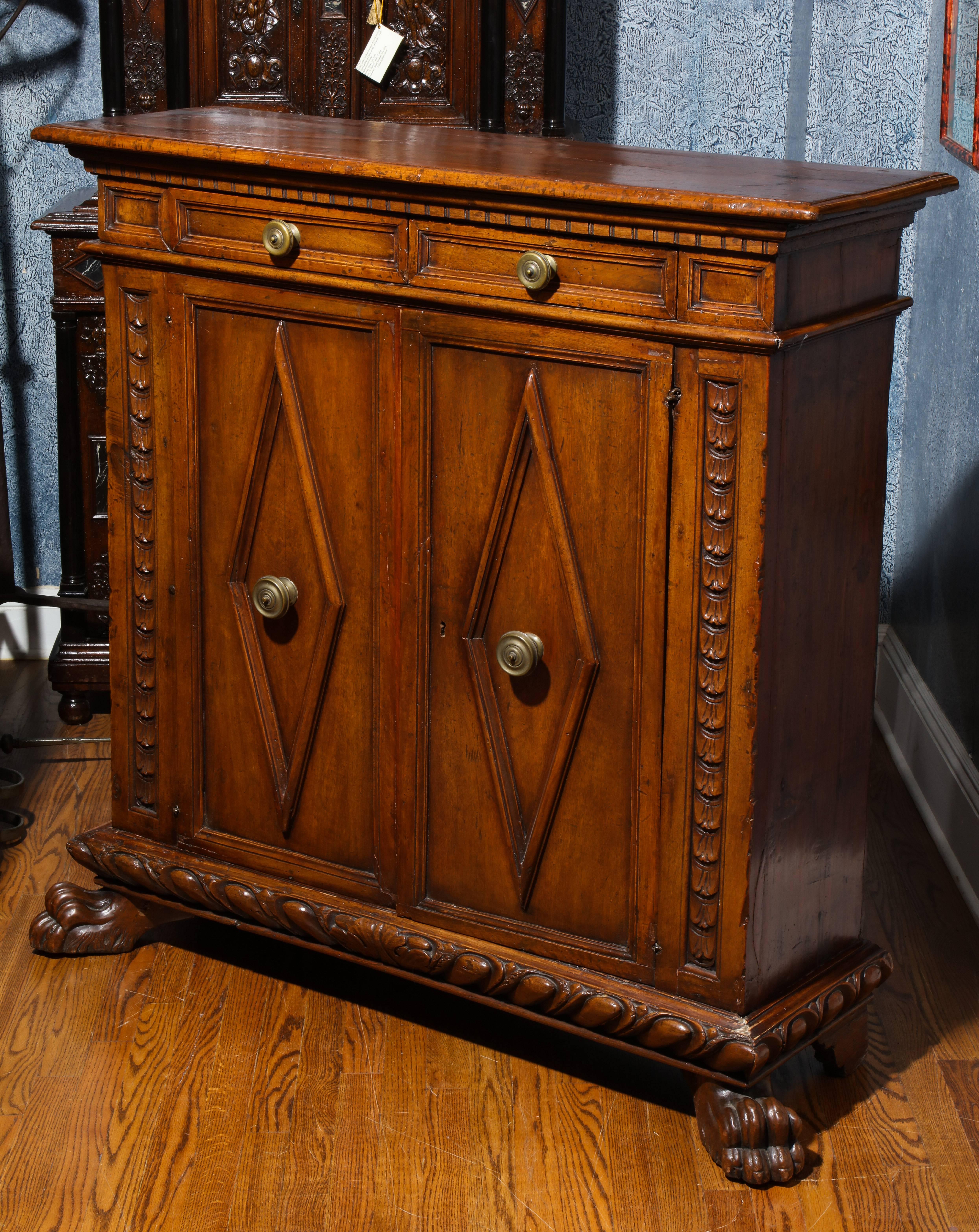 An Italian Renaissance carved walnut credenza or buffet with two doors inset with diamond form panels, below two drawers; both with large brass knobs; the whole resting on majestic carved paw feet. The frieze with dental carved molding and two front