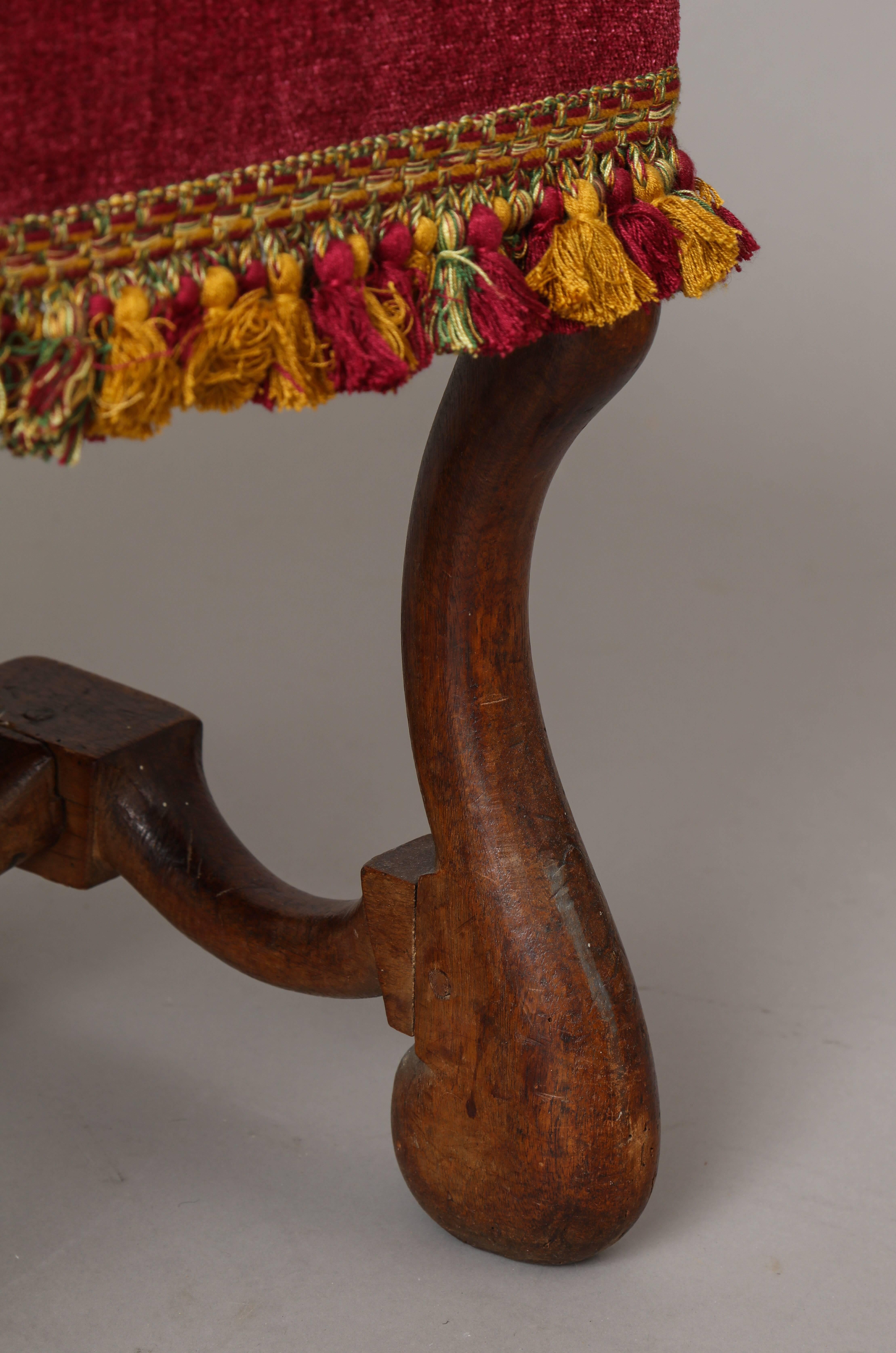 A Louis XIII period walnut bench/stool with ‘Os de mouton’ legs and a conforming stretcher, upholstered in magenta velvet with ochre and magenta silk tassels.
France, 17th century.
    
    