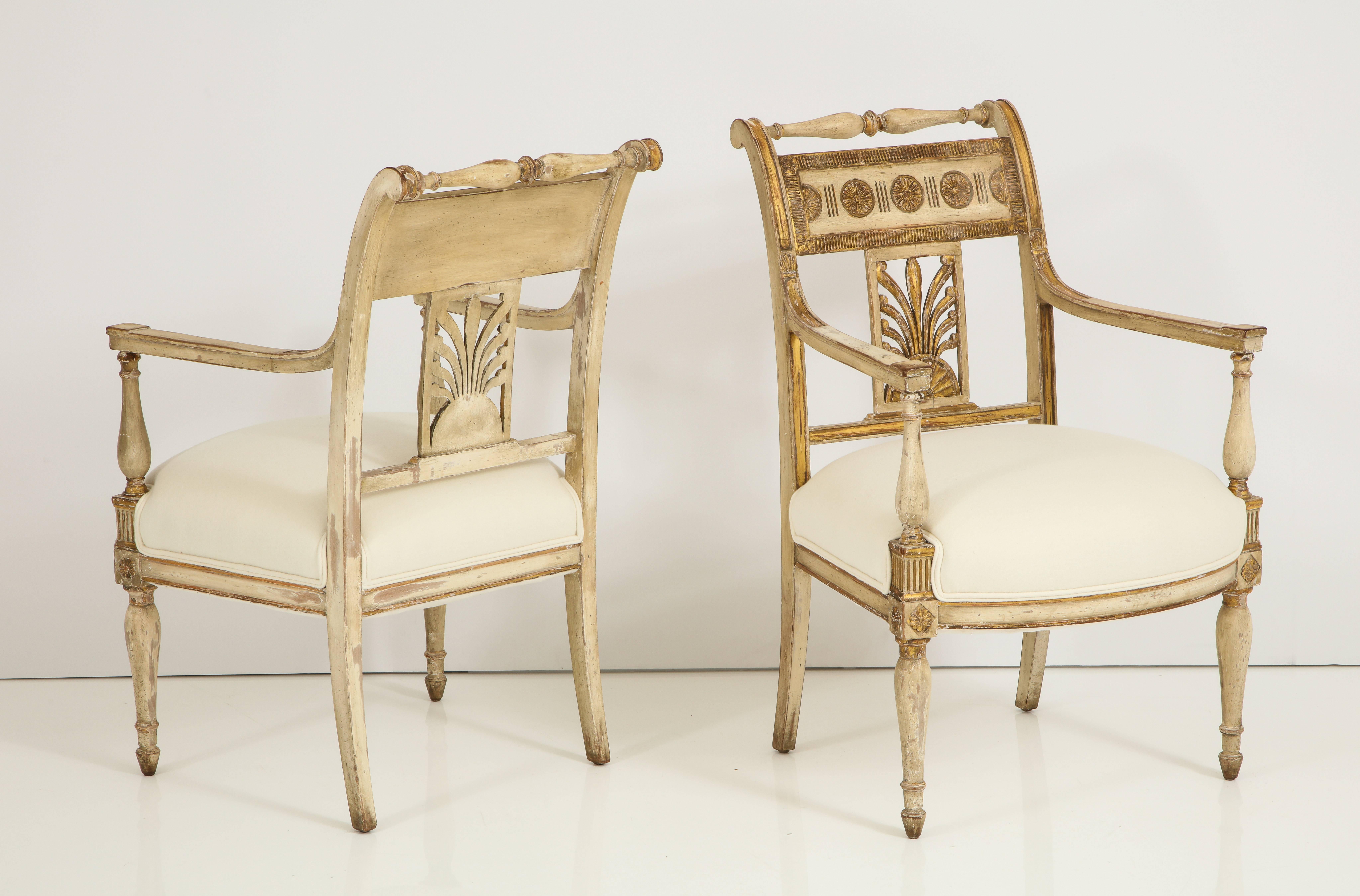 A stunning pair of Italian Neapolitan Empire period carved, painted and parcel gilded armchairs. The backrest with gilded roundels and a central carved fan motif; with carved and gilded rosettes on the headed tapered shaped legs. Newly upholstered