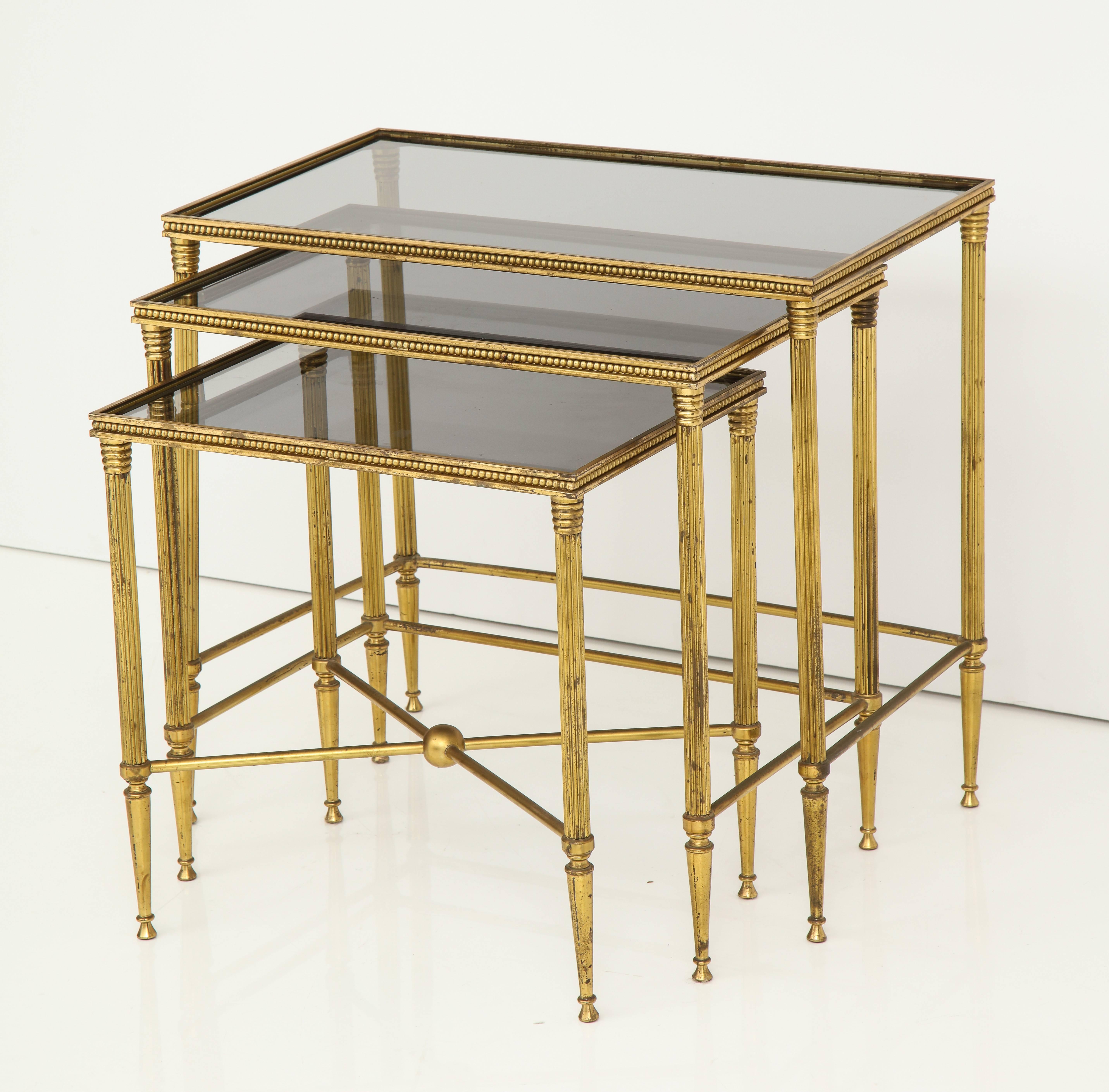 A stylish set of Italian nesting tables in brass, the legs tapered and fluted with the smallest of the three tables having a cross-stretcher. The apron with beaded decoration all around. The inset tops with smoked glass.
Italy, circa 1960
Size: 21