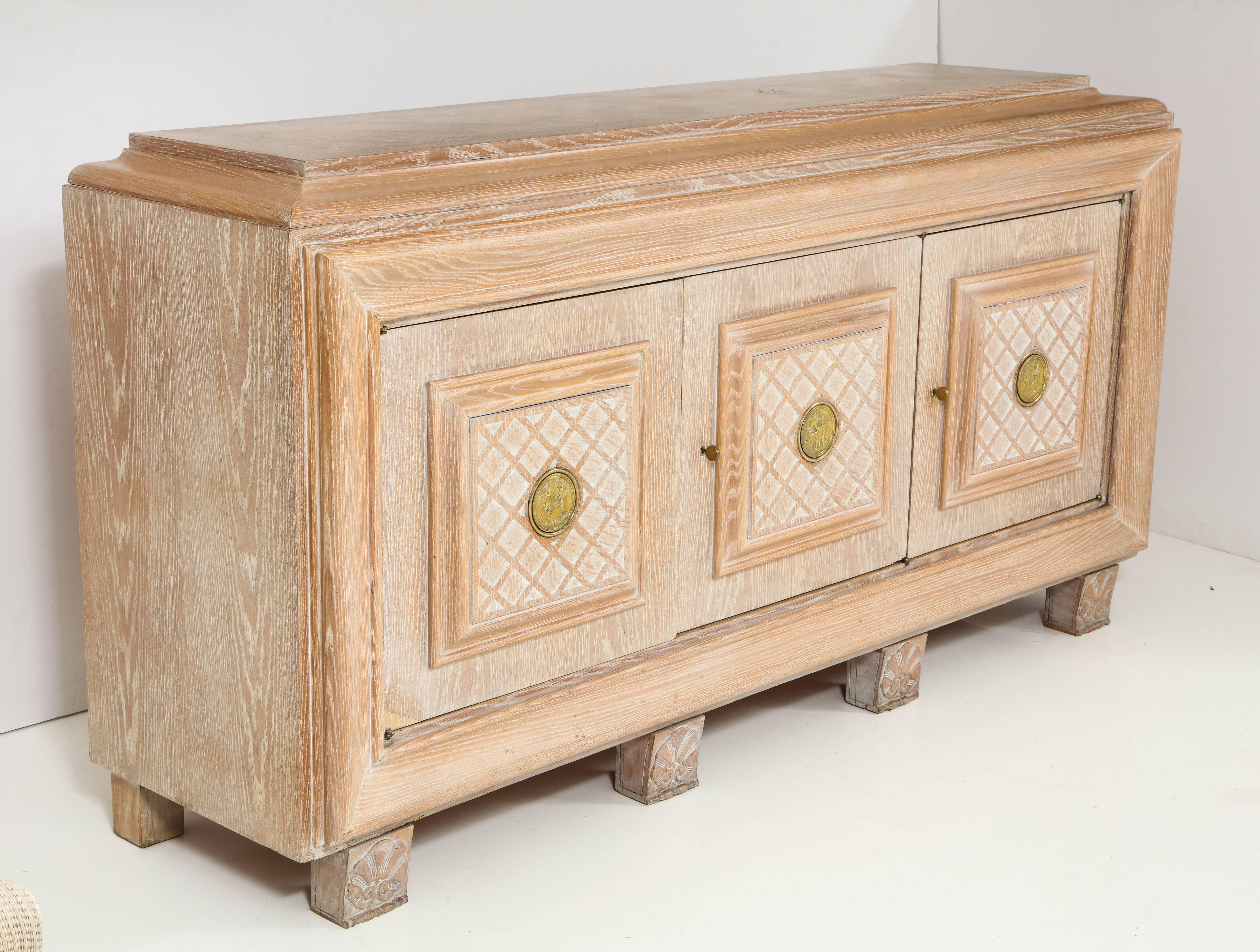 A French Art Deco cerused oak sideboard with three doors with carved cross hatch design; the case resting on four square block carved supports with shell motif.  The two outer doors  open to reveal two shelves, the central door with a top shelf