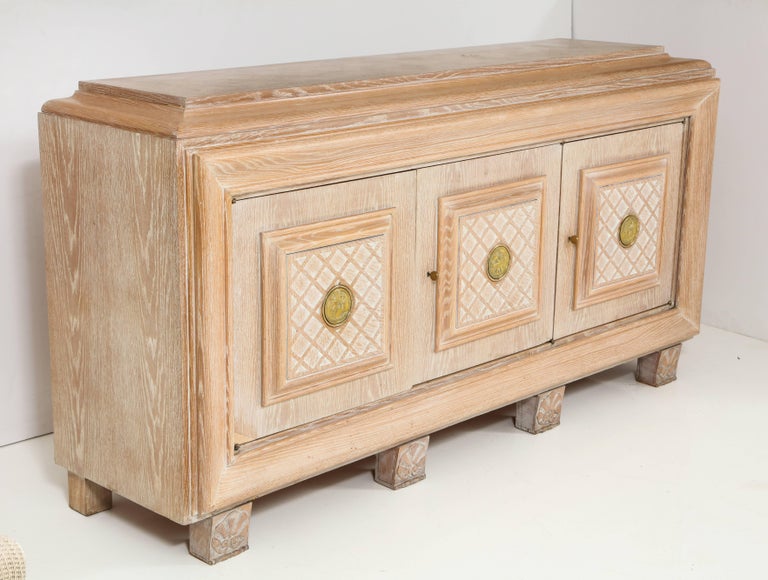 A French Art Deco cerused oak sideboard with three doors with carved cross hatch design; the case resting on four square block carved supports with shell motif.  The two outer doors  open to reveal two shelves, the central door with a top shelf