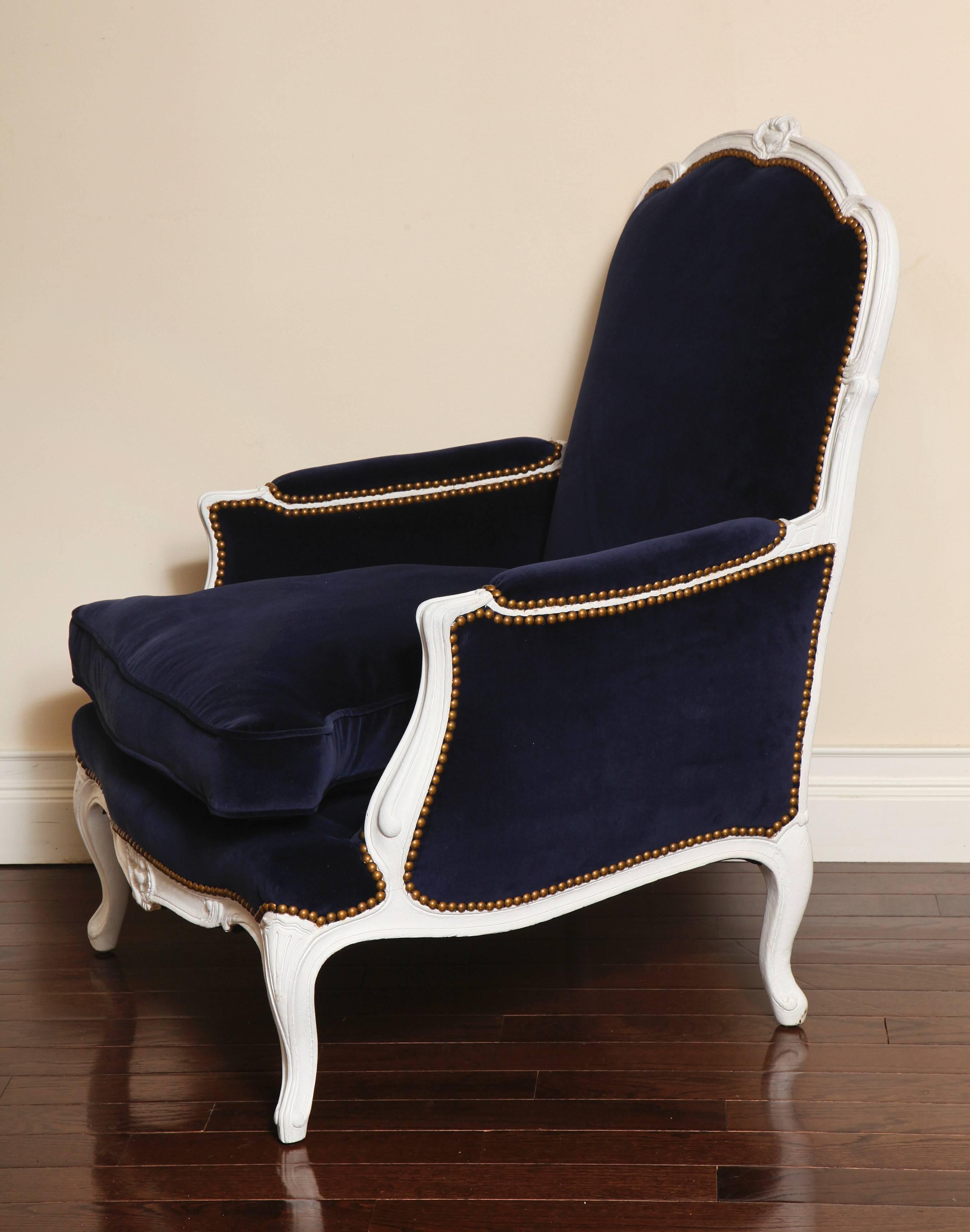 A beautifully proportioned French Louis XV style 19th century painted white bergère. The frame with cabriole legs and nicely carved cartouches on the crest and seat rail. The chair is newly upholstered in a rich dark blue velvet with antique brass