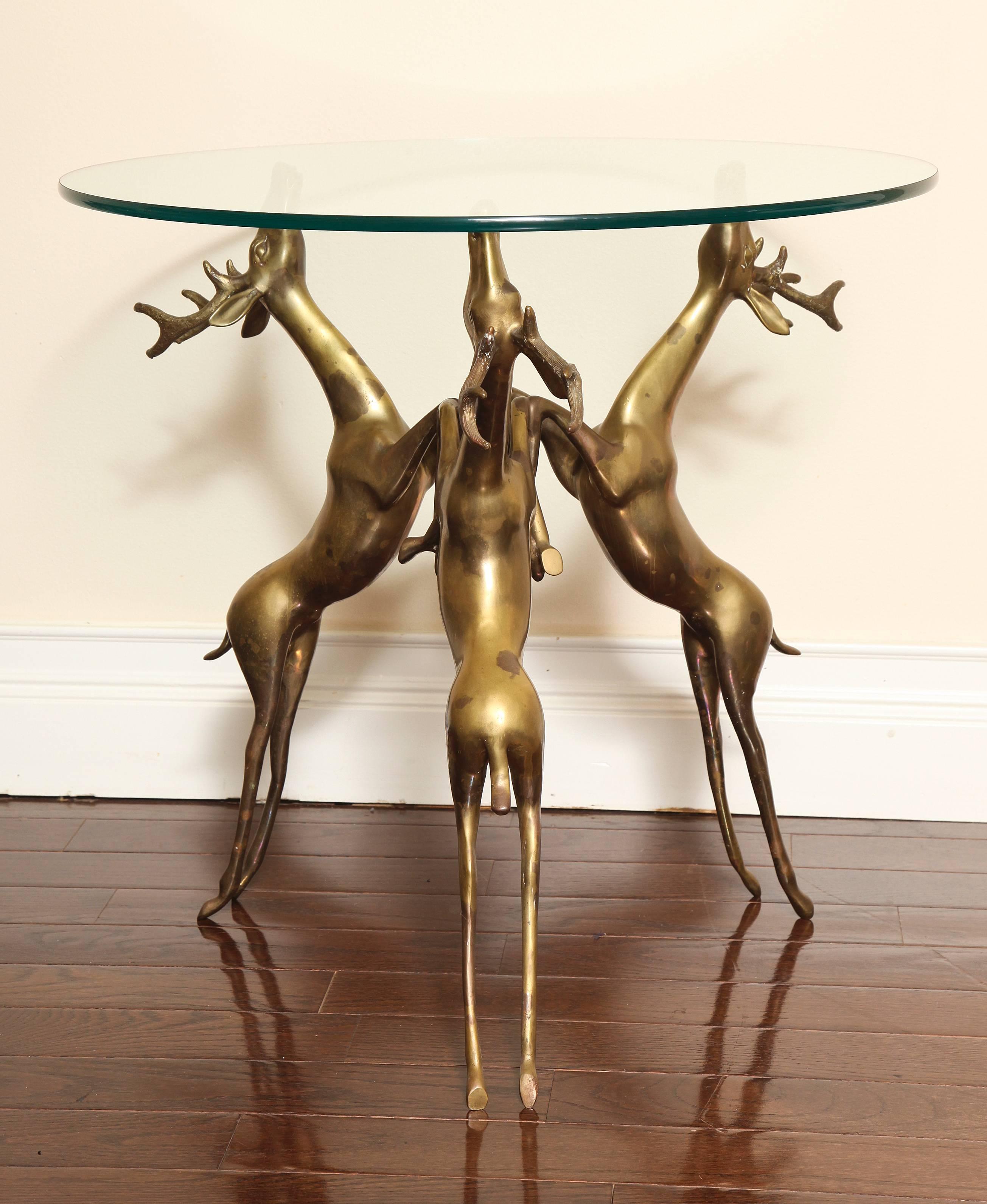 A circular glass top coffee or side table; the support base with three bronze rearing deer which is heavy and very sturdy.