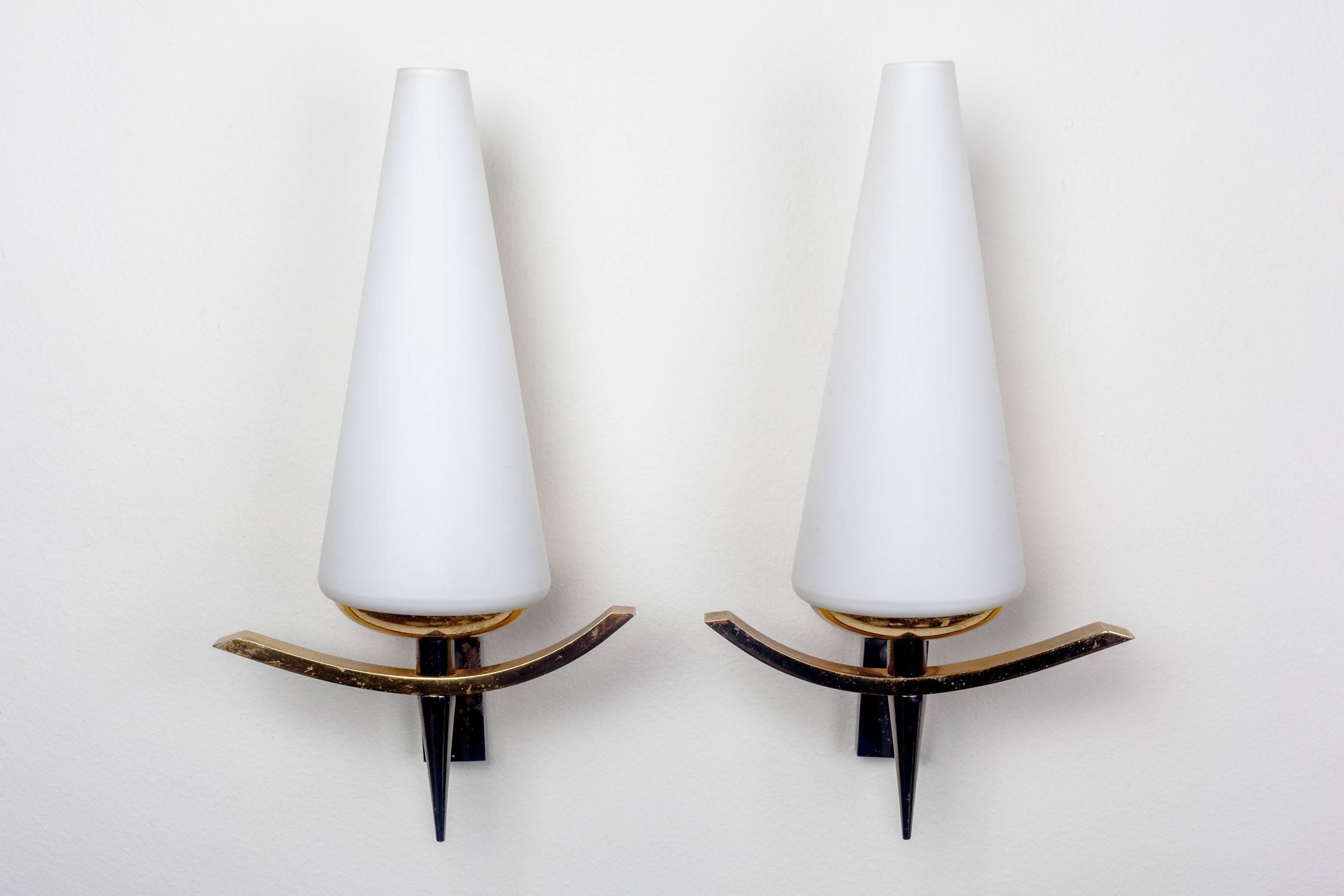 Mid-century French sconces with conic, opaline glass shades, and dark metal and brass bases in distinctive cross bow shape. Each having a significant weight, these two vintage wall lamps are robust. They will enrich their environment with their