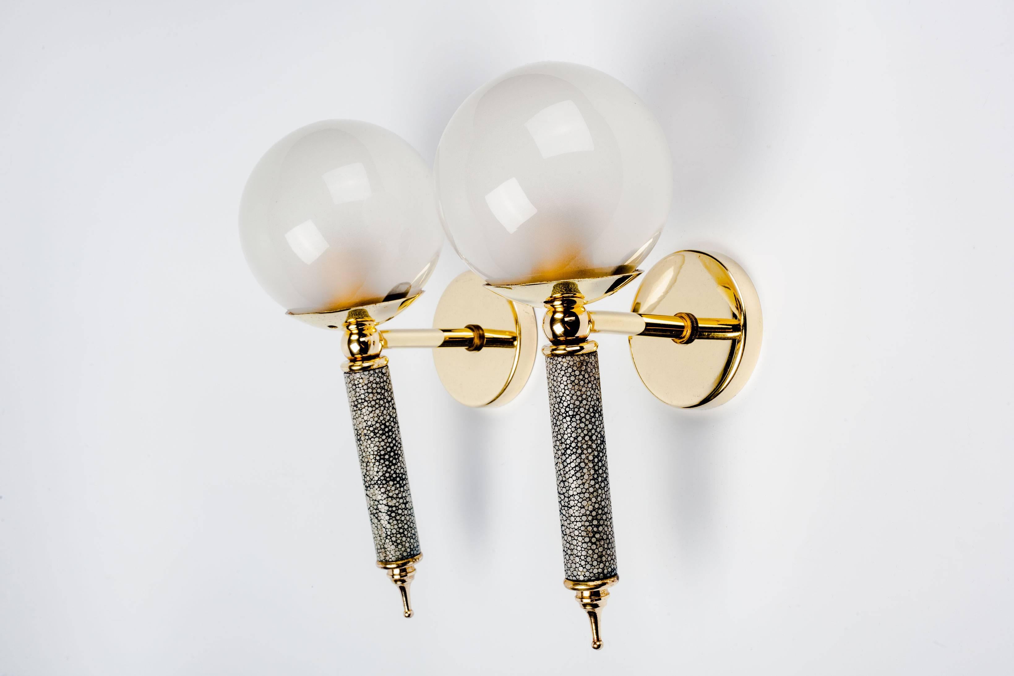 Midcentury French brass sconces with round, opaline glass diffusers. Interior frosting on the glass orbs cast a glowing light. Stems are covered in shagreen. 

Shagreen, wrapped around the stems of these sconces, is leather-like to the touch. Called